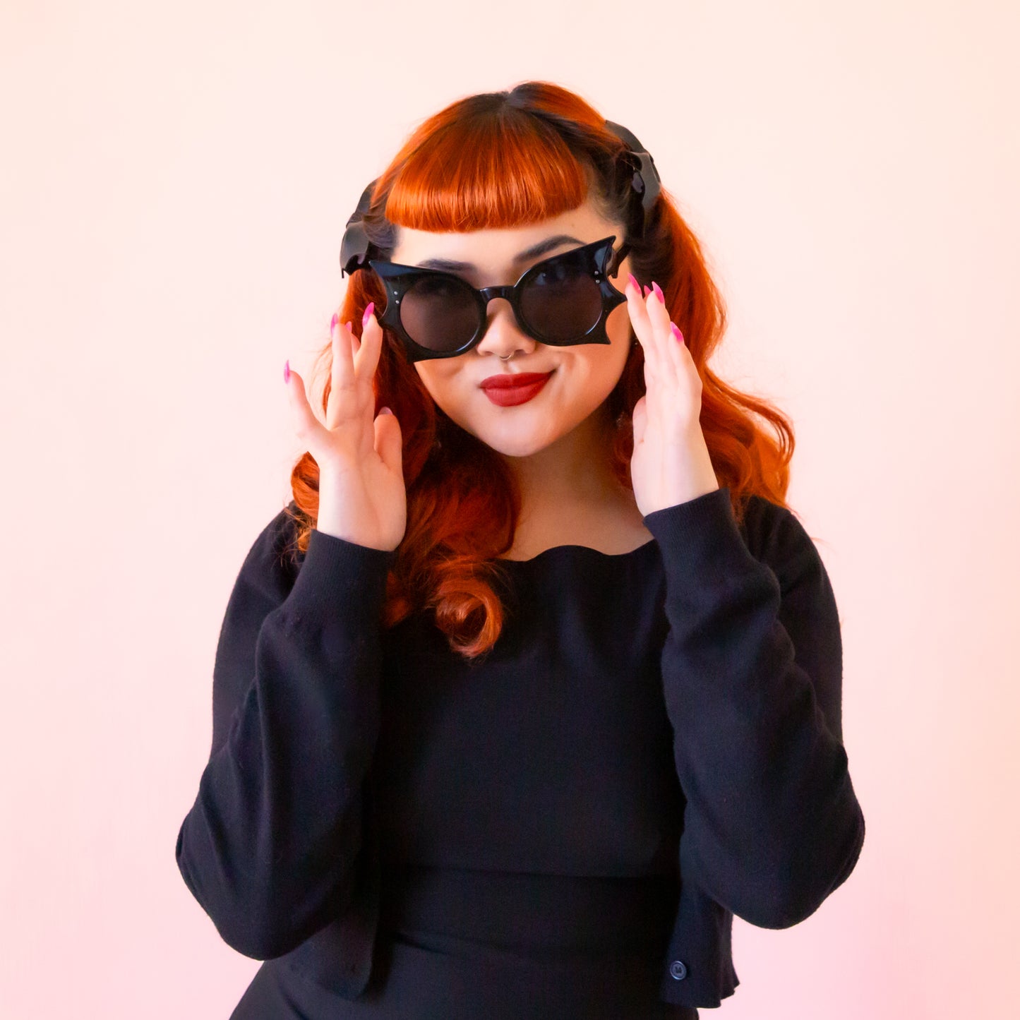 A red headed model wears black bat wing shaped sunglasses.
