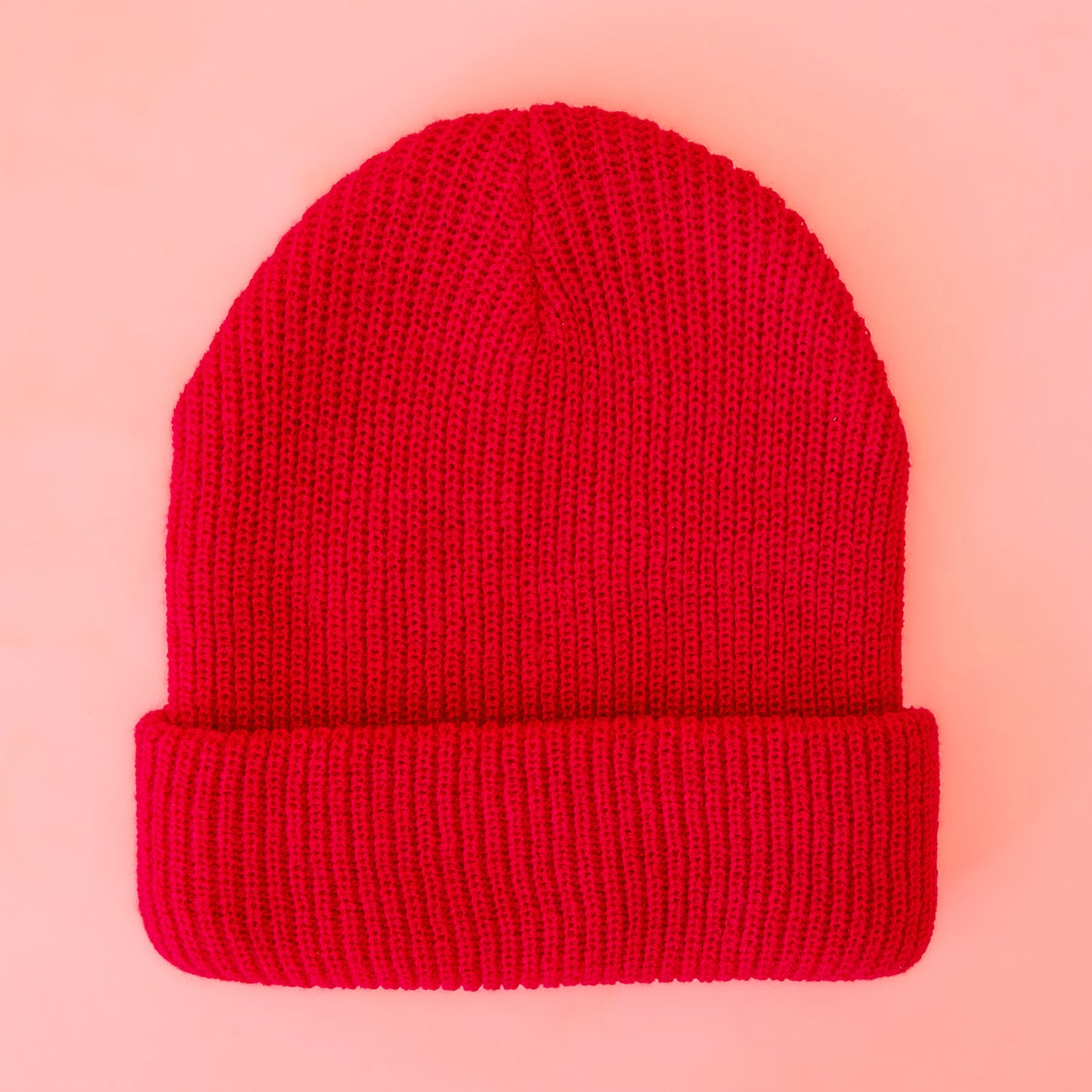 A bright red knit beanie sits on a peach colored ground.