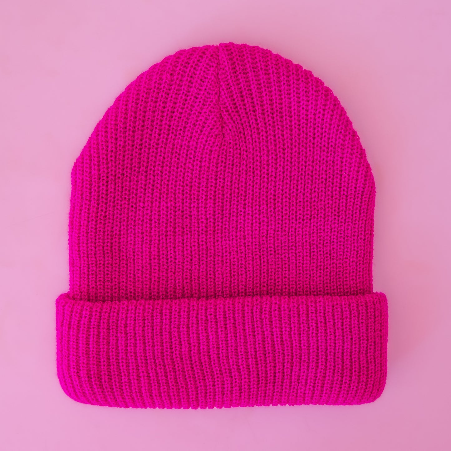 A hot pink knit beanie sits on a pink background.