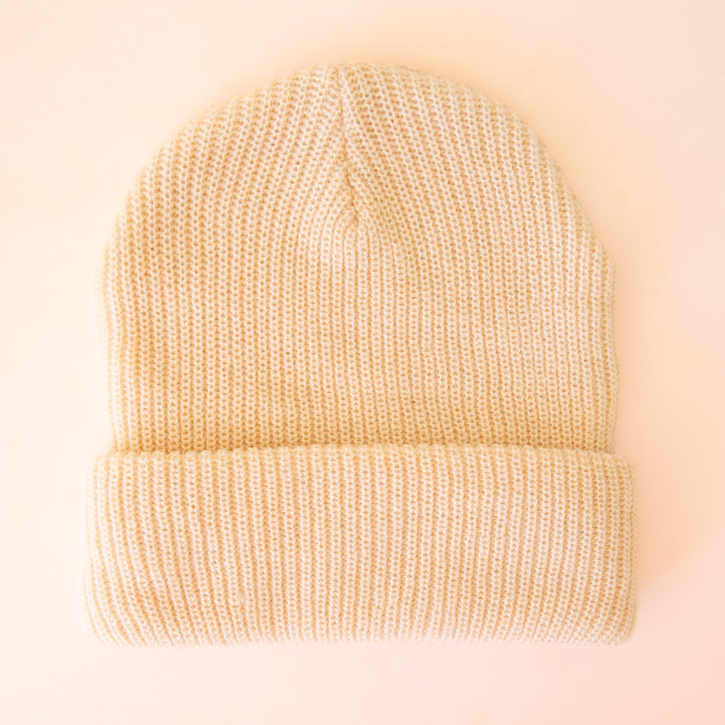 A cream colored knit beanie sits on an ivory background.