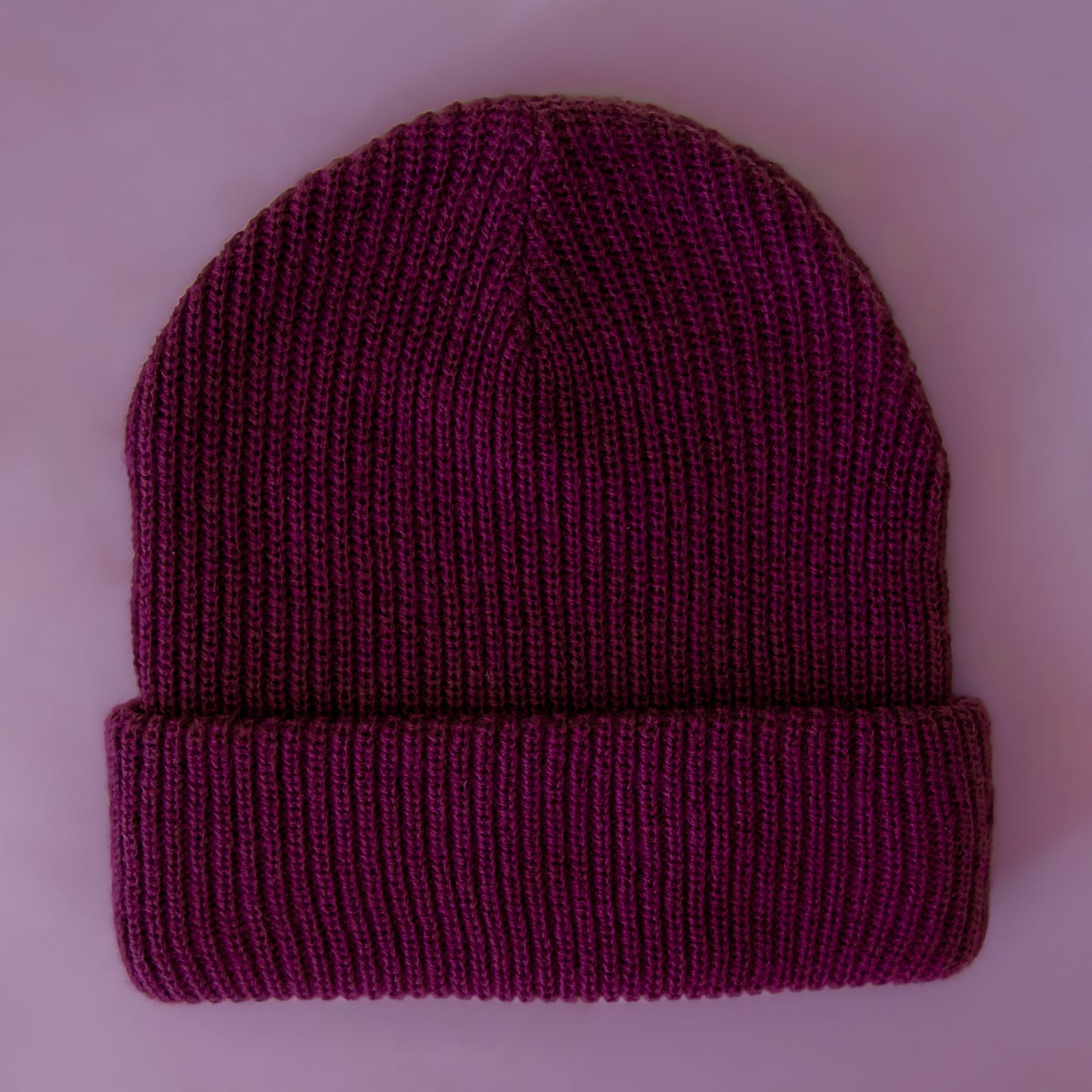 A knit beanie in an aubergine color sits on a lavender background.