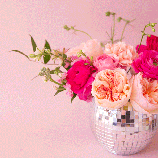 A round disco ball hanging planter with a 6" opening and a silver chain hanger photographed here with a pink flower arrangement inside. .