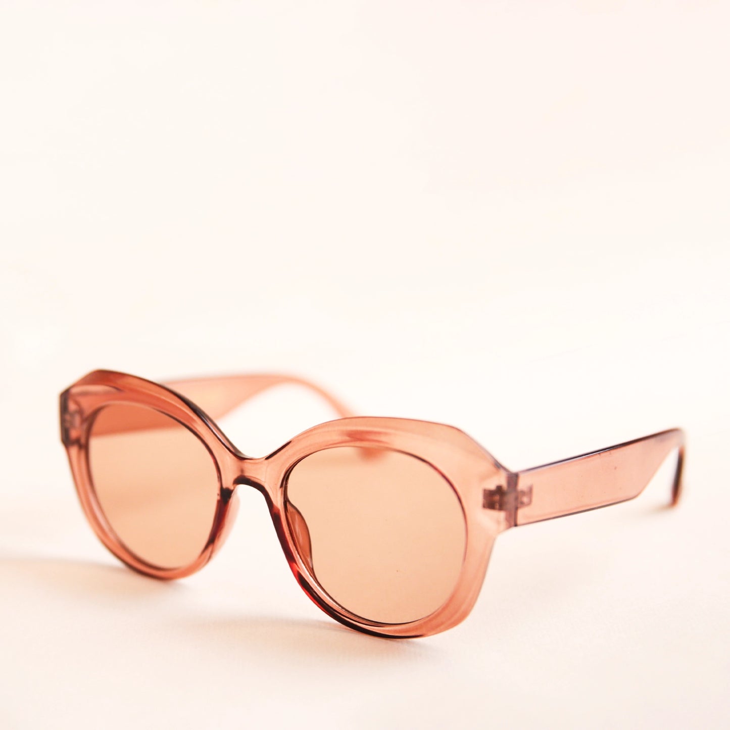 On a white background is a light brown translucent sunglasses that have a rounded shape and a light brown lens.
