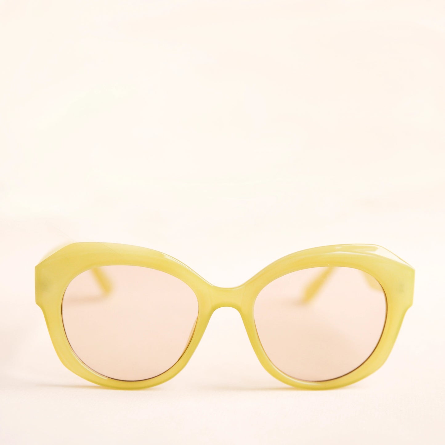 On a white background is a round pair of light green sunglasses with a light brown lens.