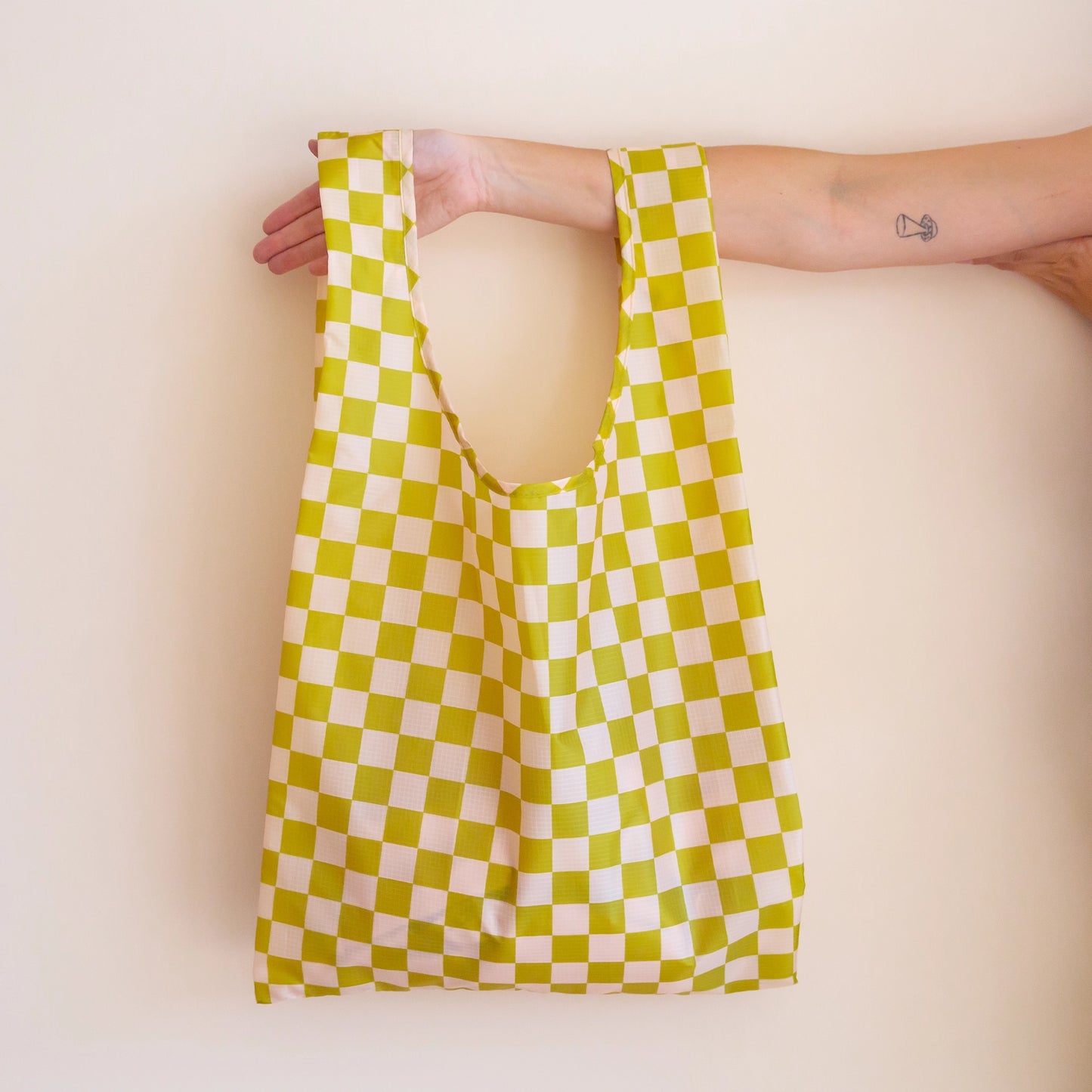 On a light pink background is light green and ivory checkered reusable nylon bag.