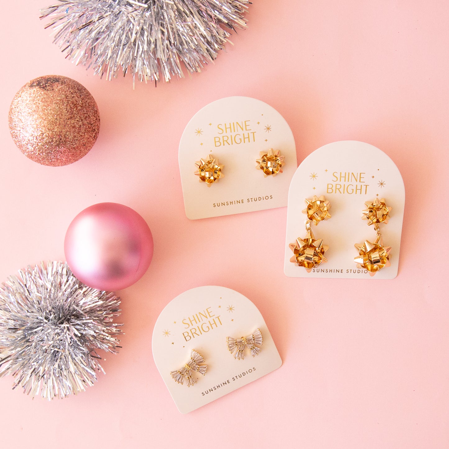 Three of our bow shaped earrings next to one another next to ornaments and tinsel.