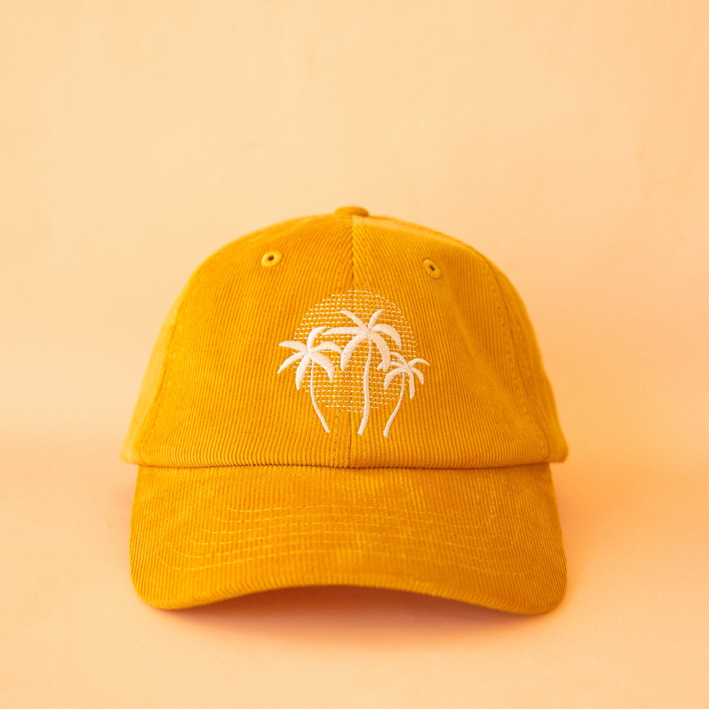 On a light yellow background is a golden yellow corduroy baseball hat with a white palm tree design in the center.