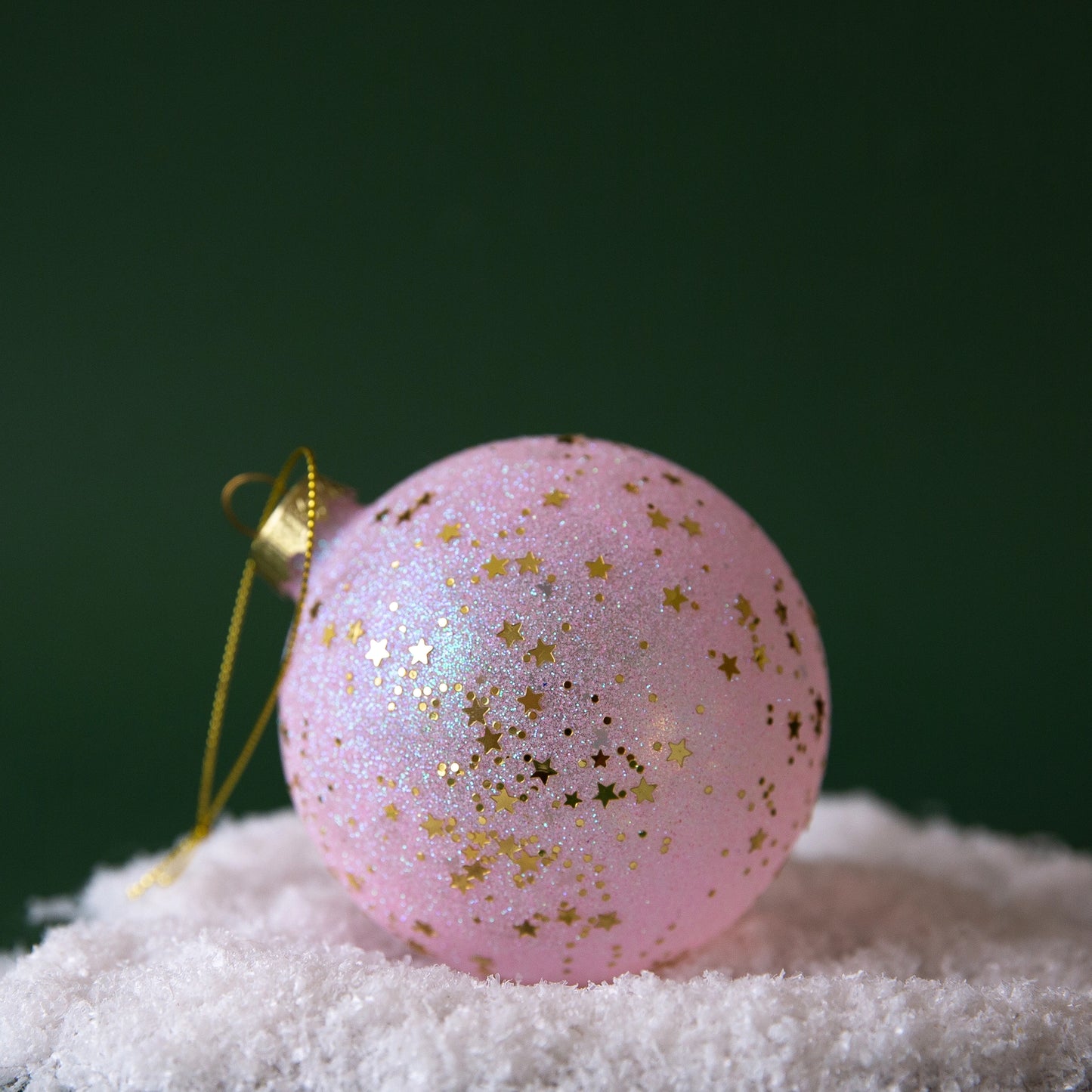 On a dark green background is a light pink and gold star ornament.