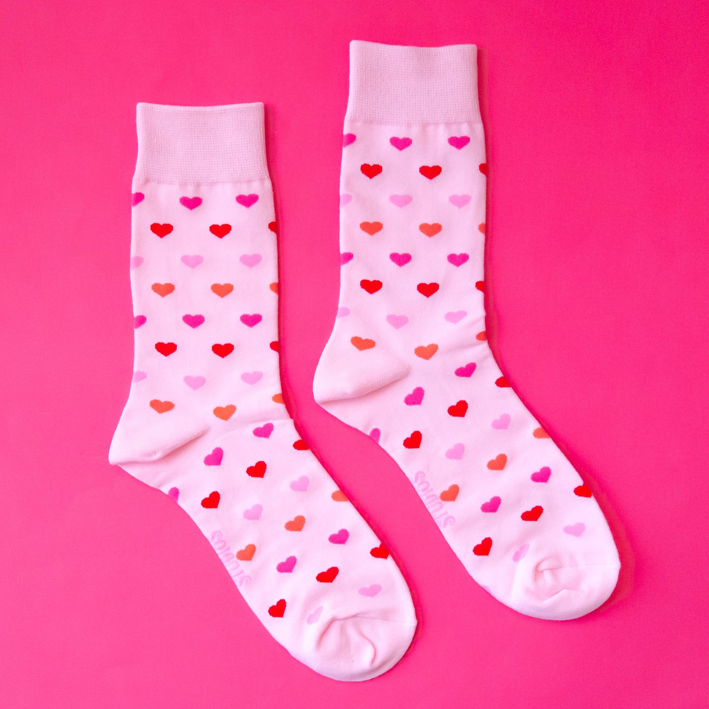 A pair of crew socks with a heart print that is in different shades of pink.