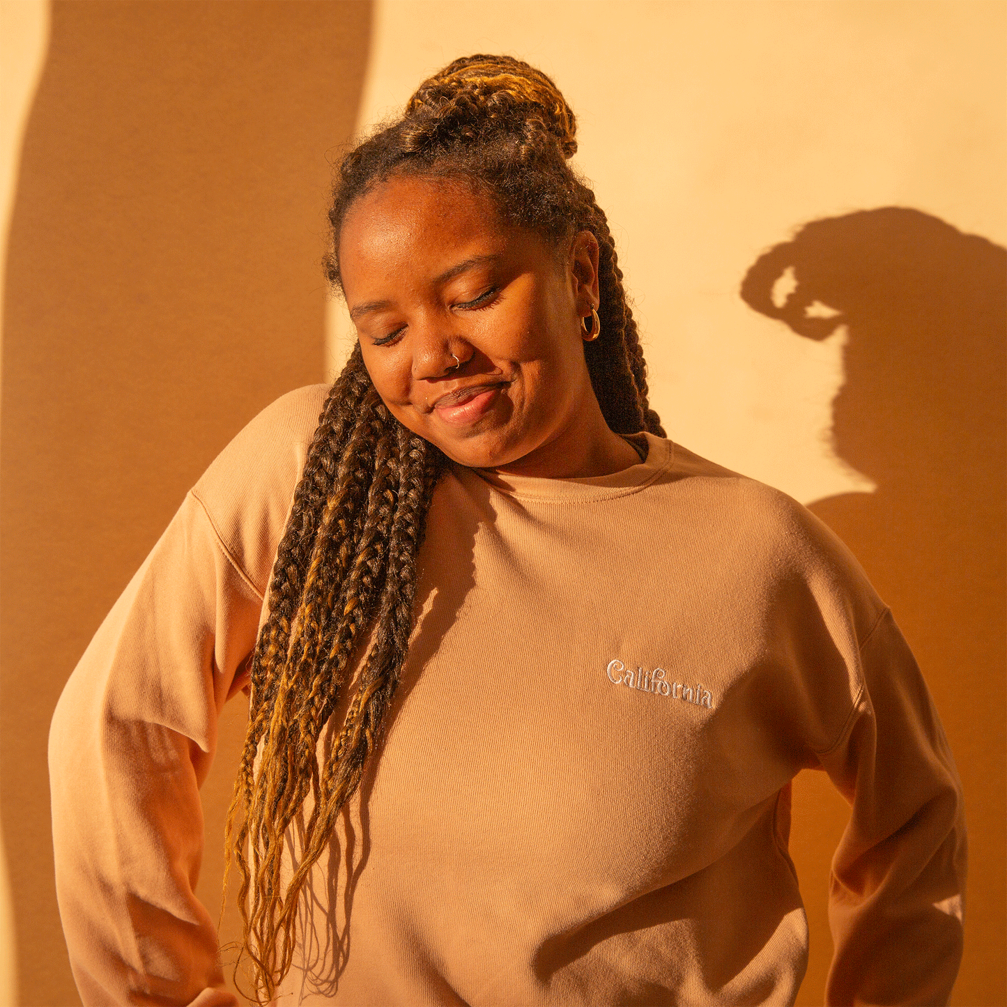 On an orange background is a peachy fleece pullover with white "California" embroidering.