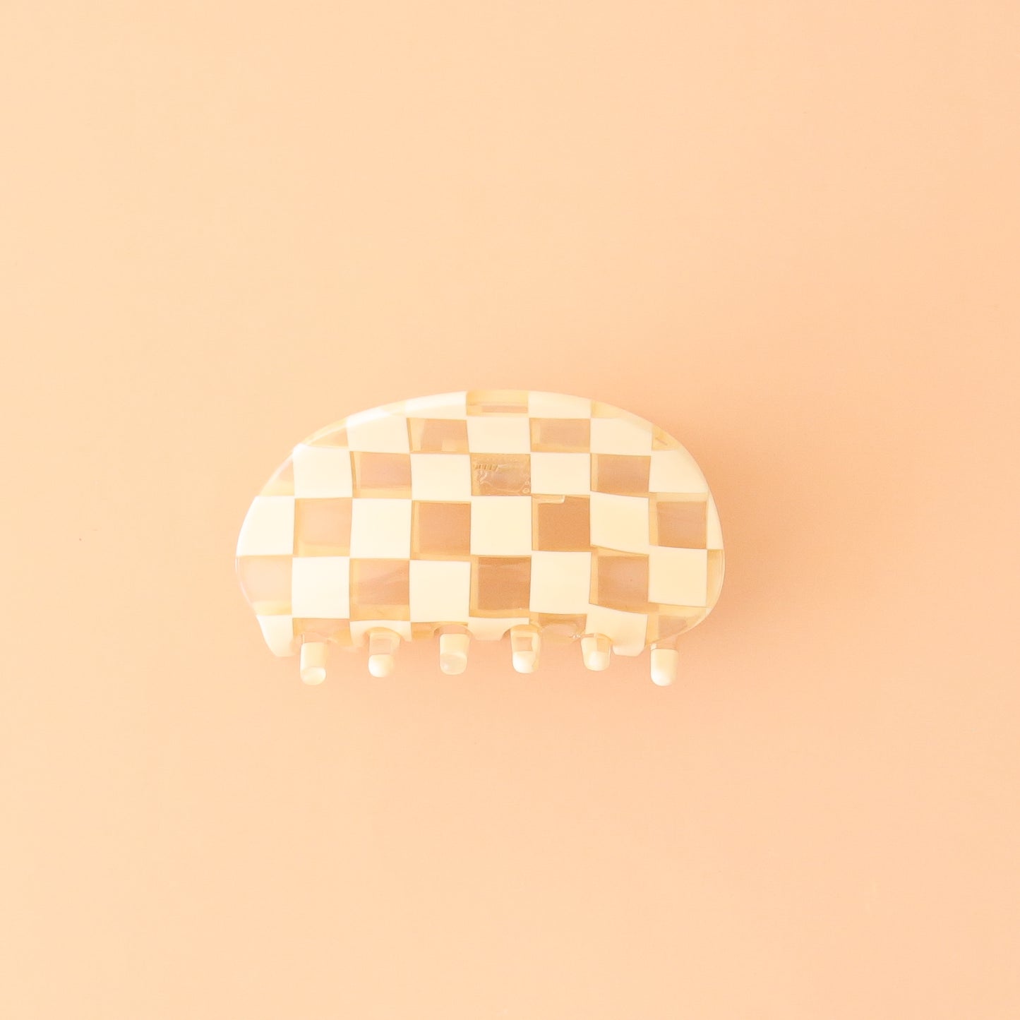 On a peachy background is an ivory and clear checker printed claw clip with a rounded edge.