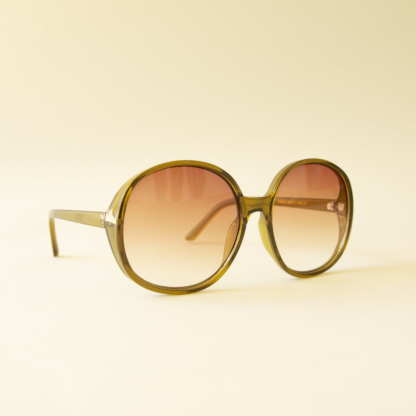 A green translucent pair of round oversized sunglasses with a light brown / pink lens.