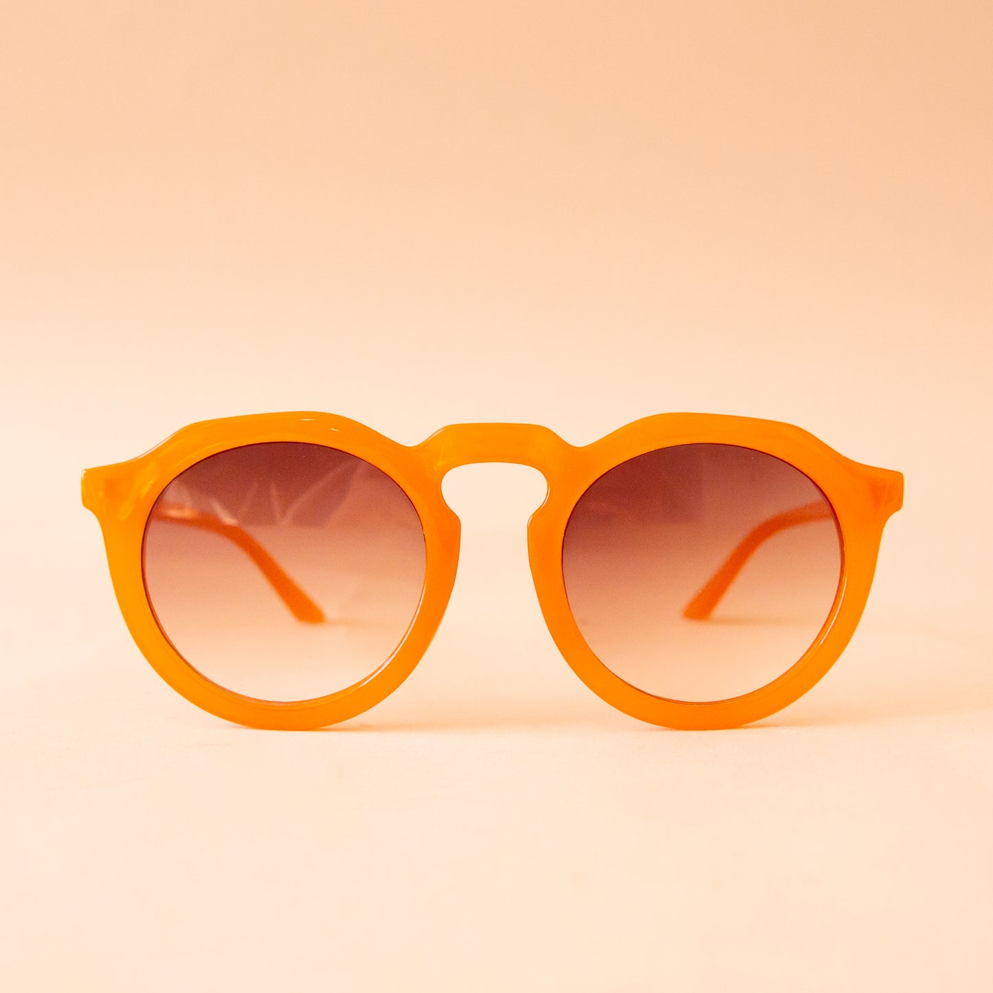 A pair of orange round sunglasses with a brown gradient lens.