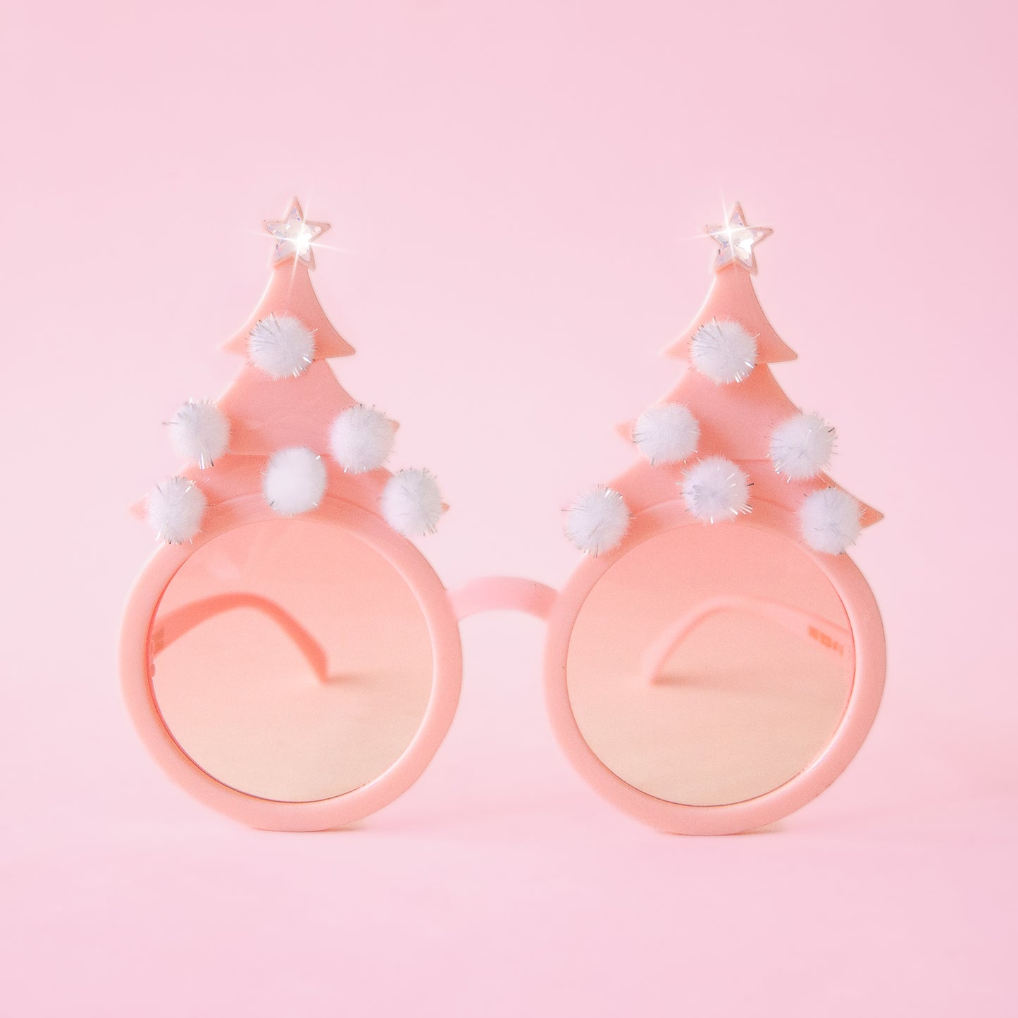 On a pink background is a pair of holiday glasses with tree shapes and six white pom poms and a star on top. Edit alt text