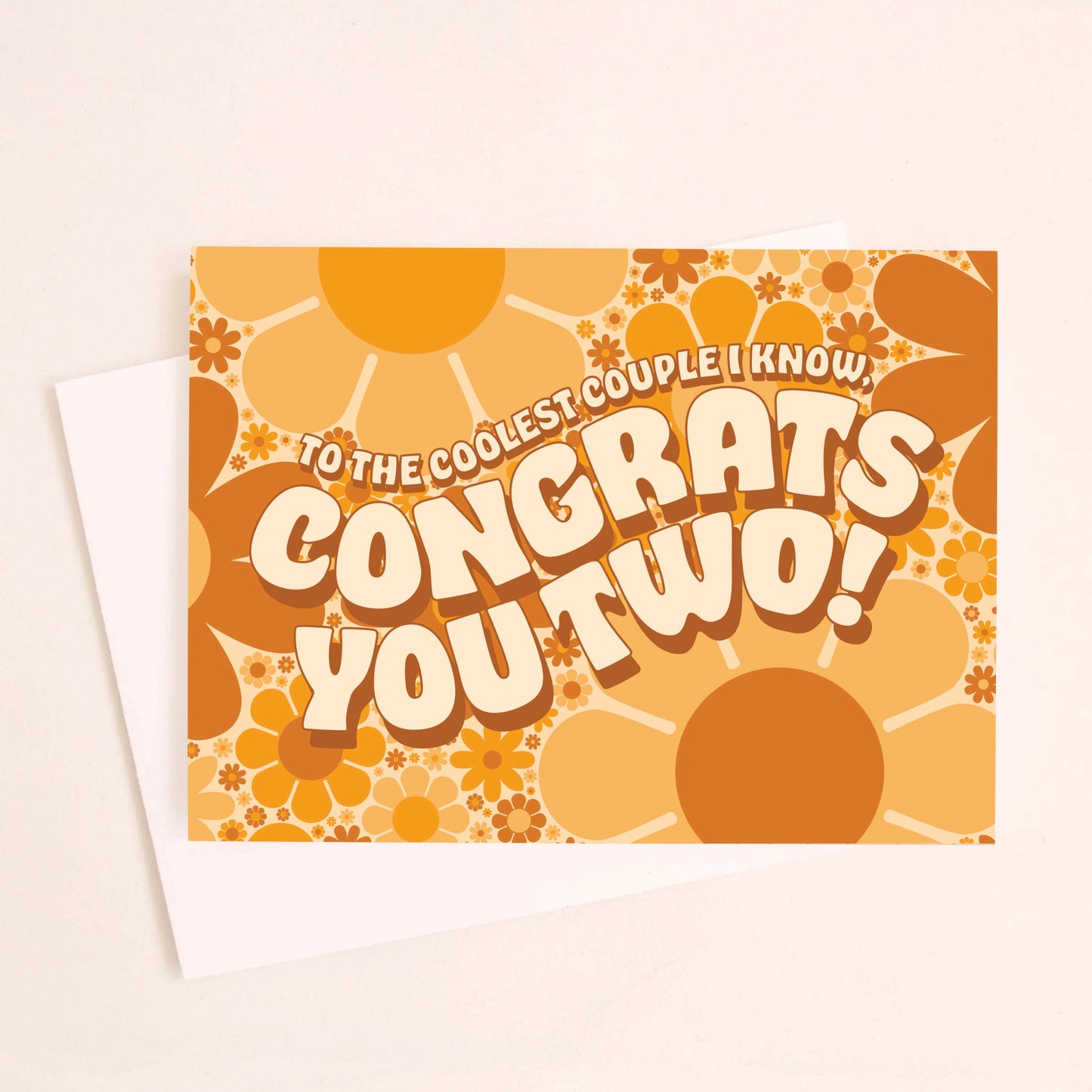 On an ivory background is a daisy print congratulations card with shades of orange and brown along with wavy text in the center that reads, "To The Coolest Couple I Know, Congrats You Two!".