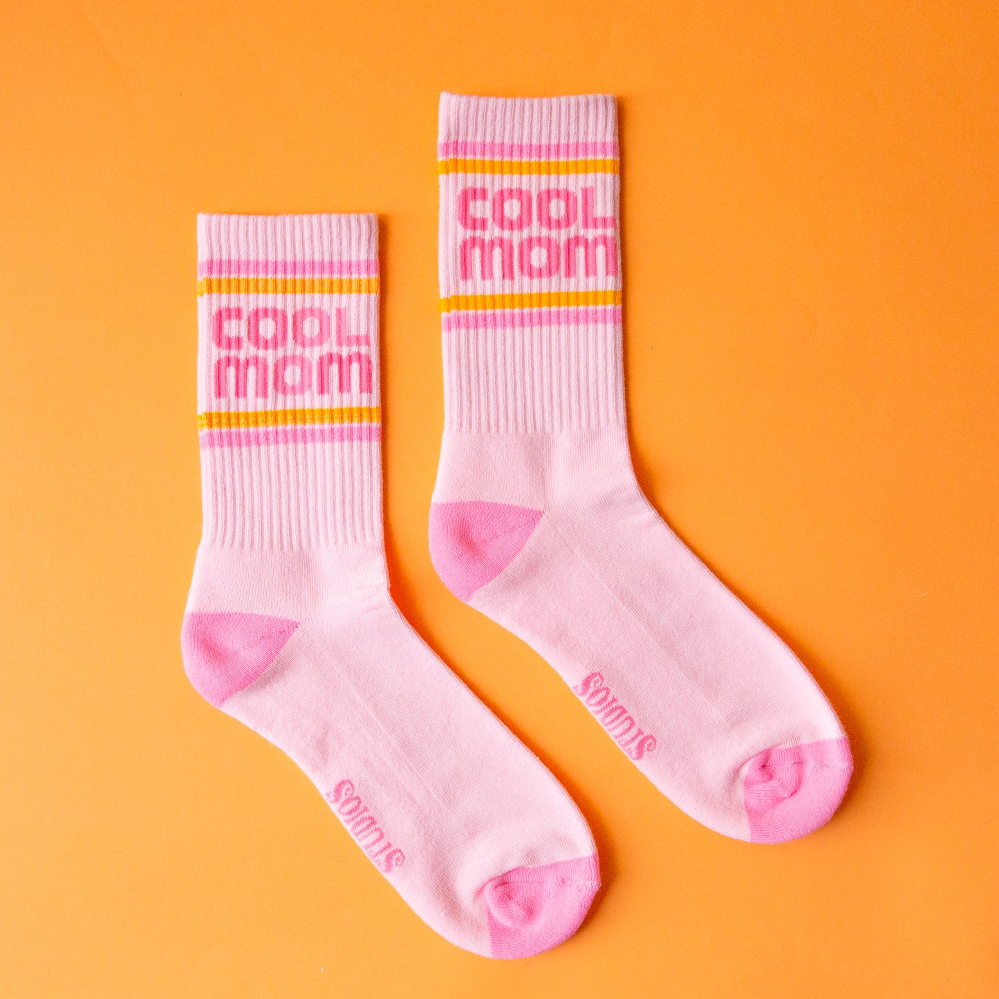 A pair of crew socks with pink and orange stripes and pink text that reads, "cool mom".