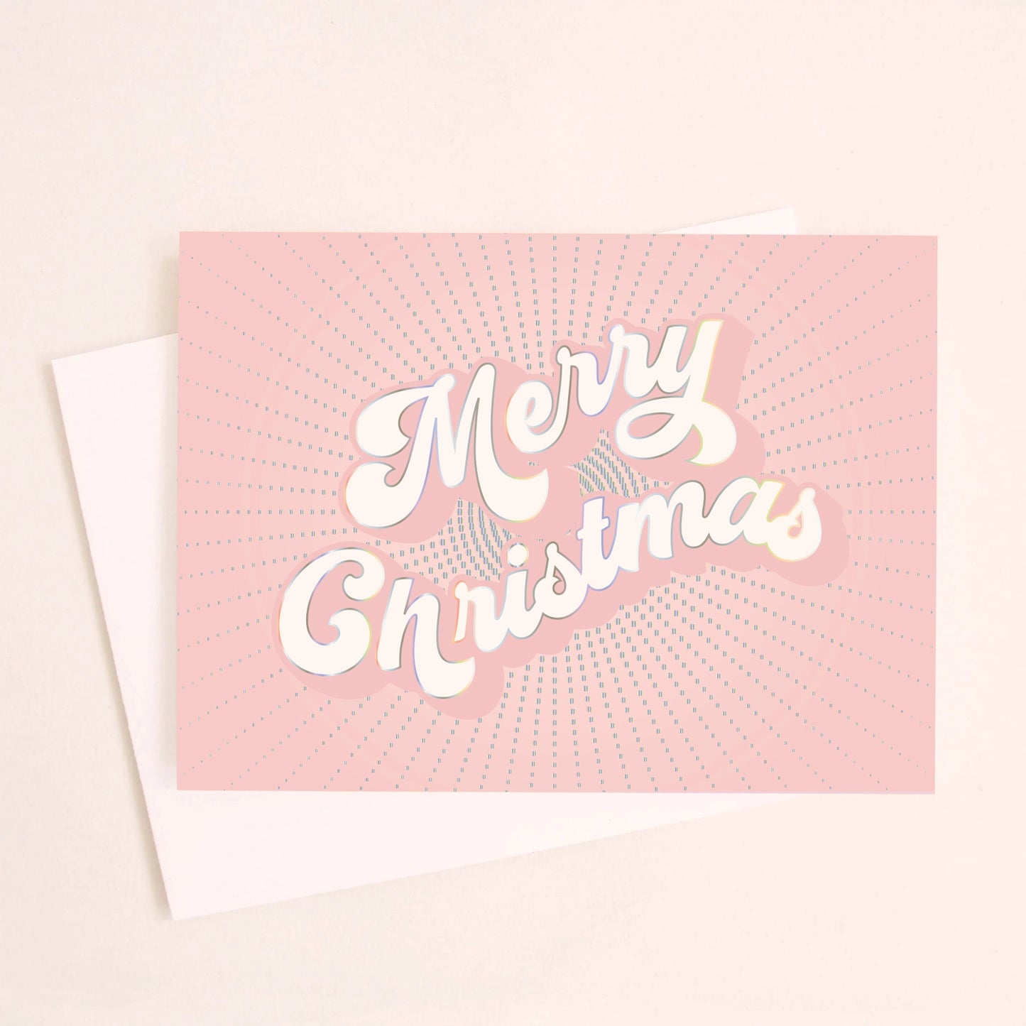 On a light pink background is a light pink greeting card with white text in the center that reads, "Merry Christmas" along with a white envelope.
