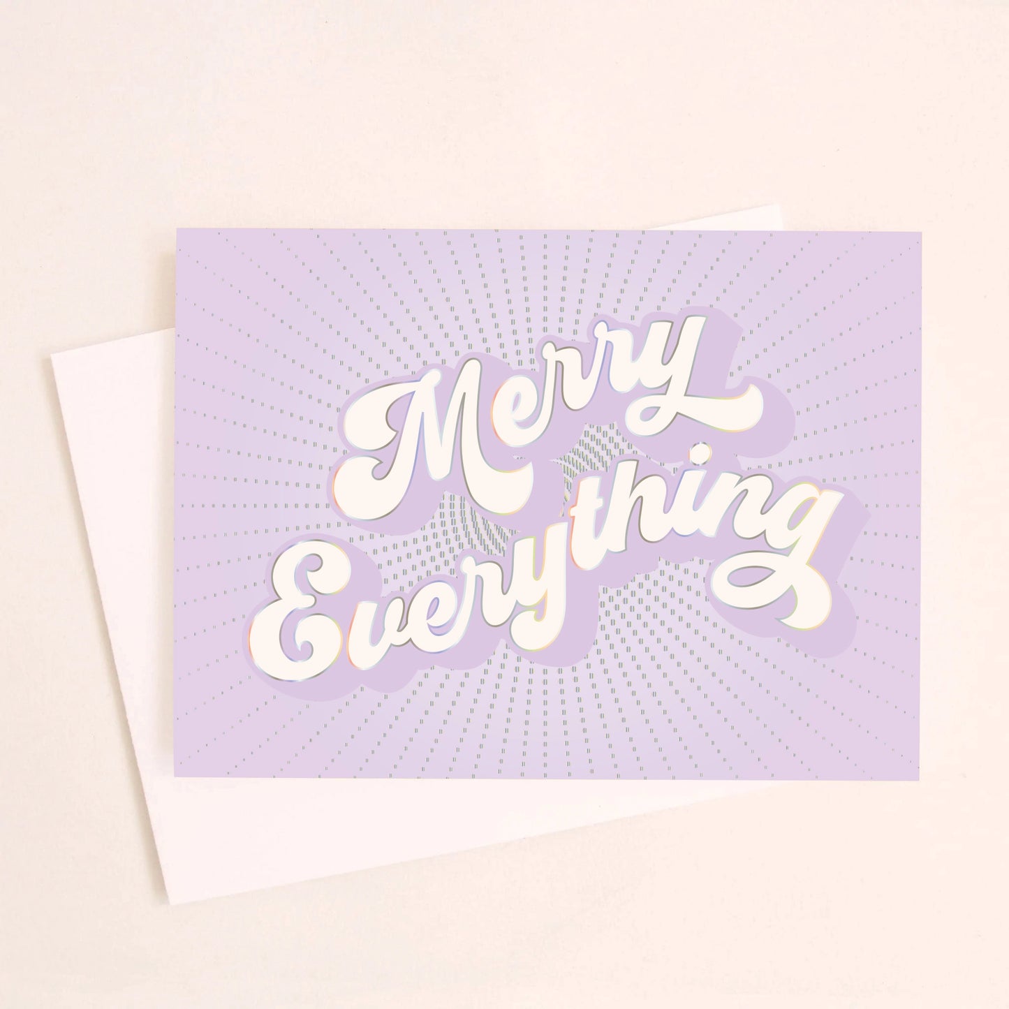 On a light pink background is a purple greeting card with white text that reads, "Merry Everything" along with a white envelope.