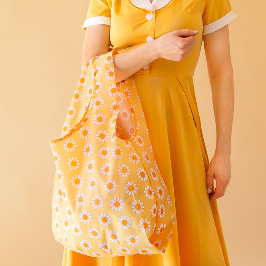 On a yellow background is a yellow, orange and white daisy pattern nylon bag. 