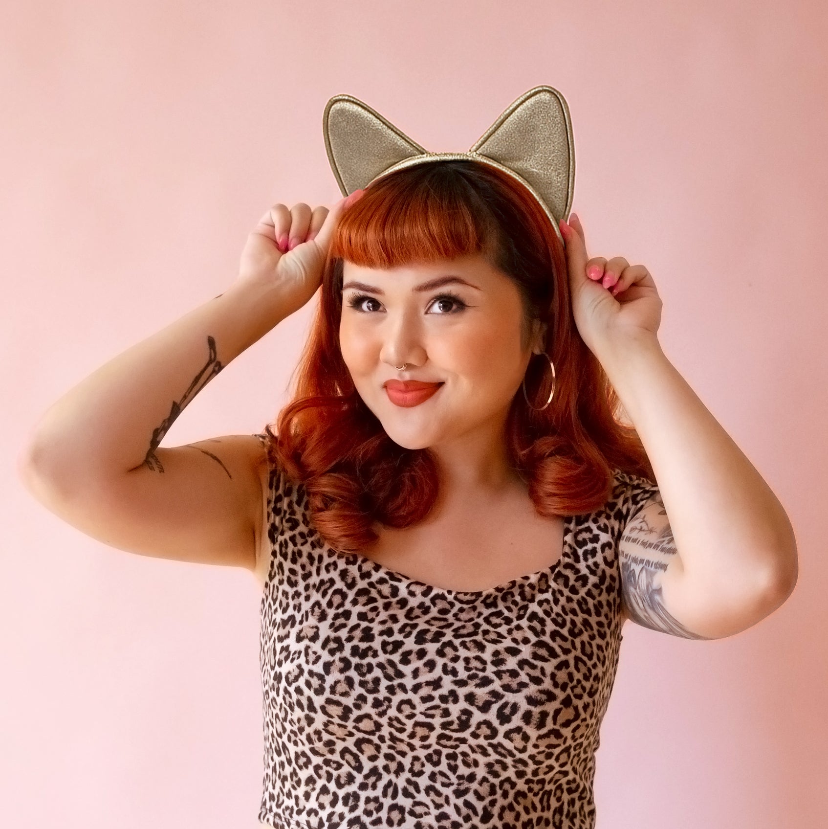 Model in leopard body suit with red hair wears a gold glitter cat ears headband.