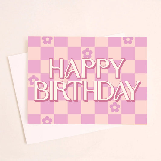 On a peachy background is a hot pink and light pink checkered greeting card with flowers in six of the checker squares along with text in the center that reads, "Happy Birthday". 