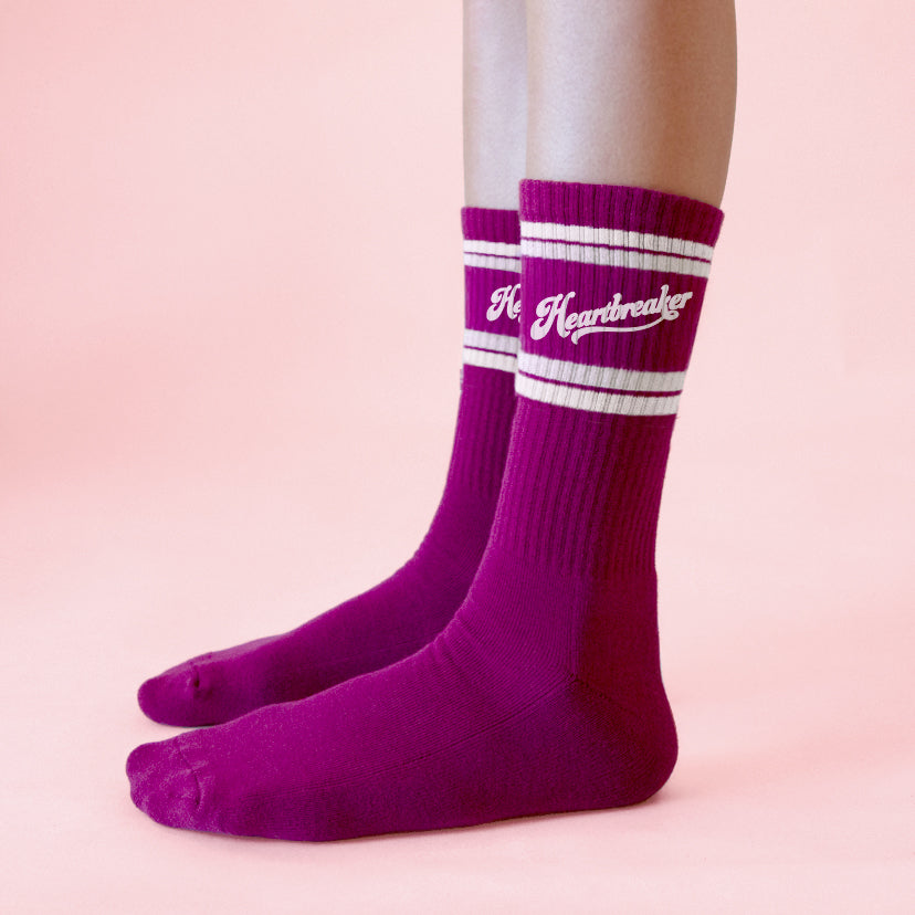 A pair of fuchsia crew socks with white "Heartbreaker" on the side.
