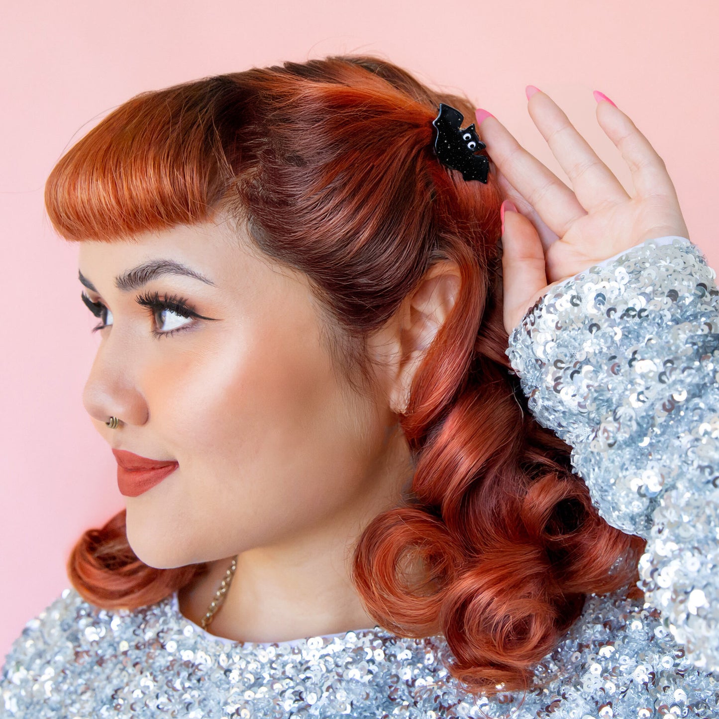 Red headed model wears a bat shaped hair clip. She is wearing a sparkly silver top.