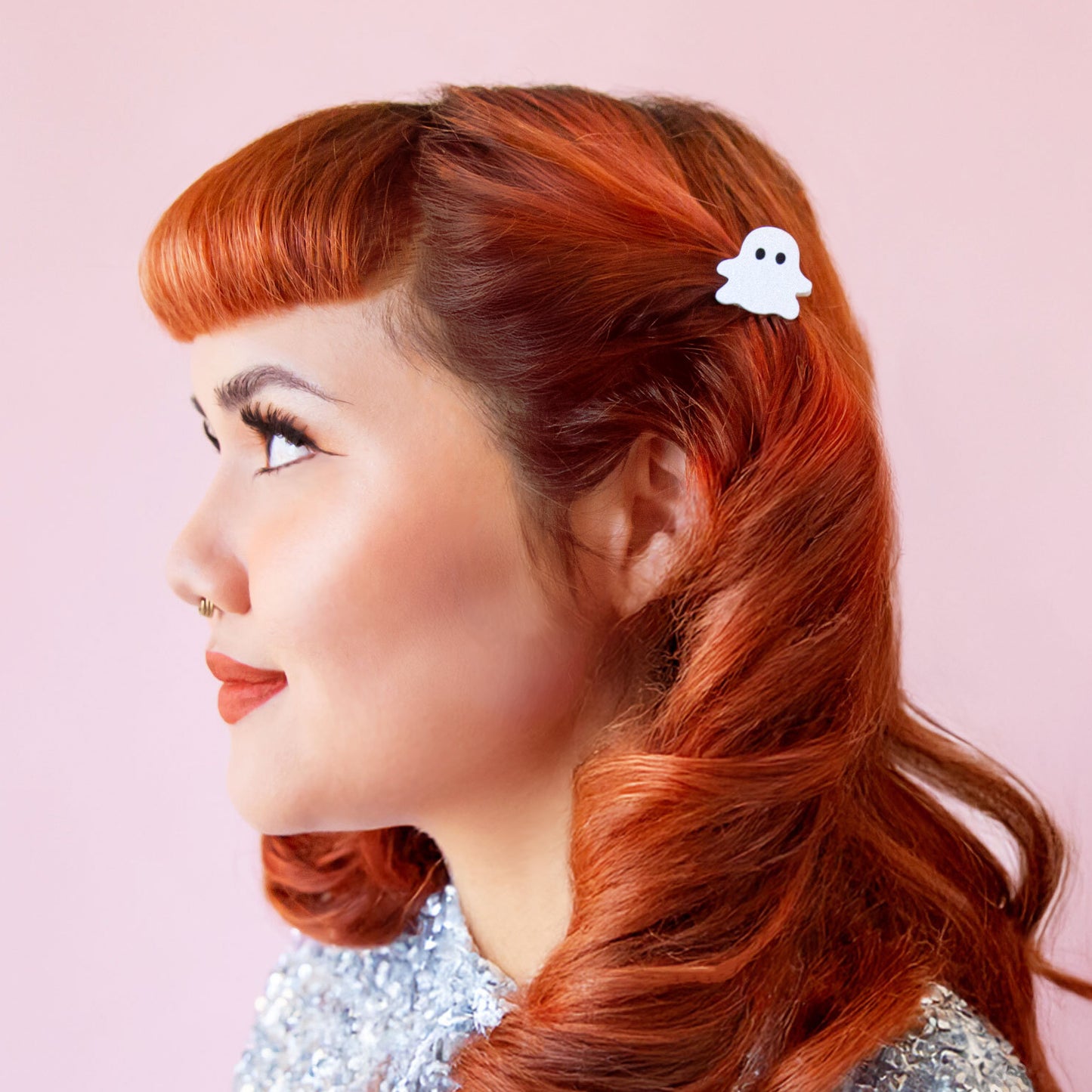 A red headed model wears a ghost shaped clip in her hair. She has soft curls and red lipstick on.