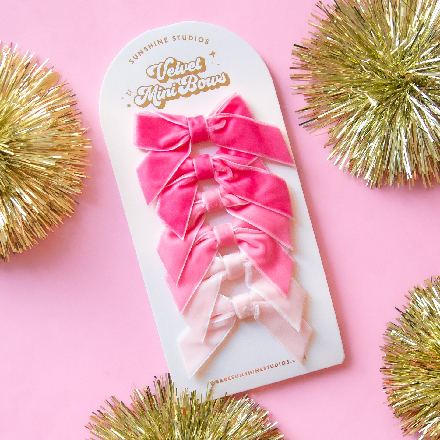 On a pink background is a set of velvet bows in three different shades of pink.