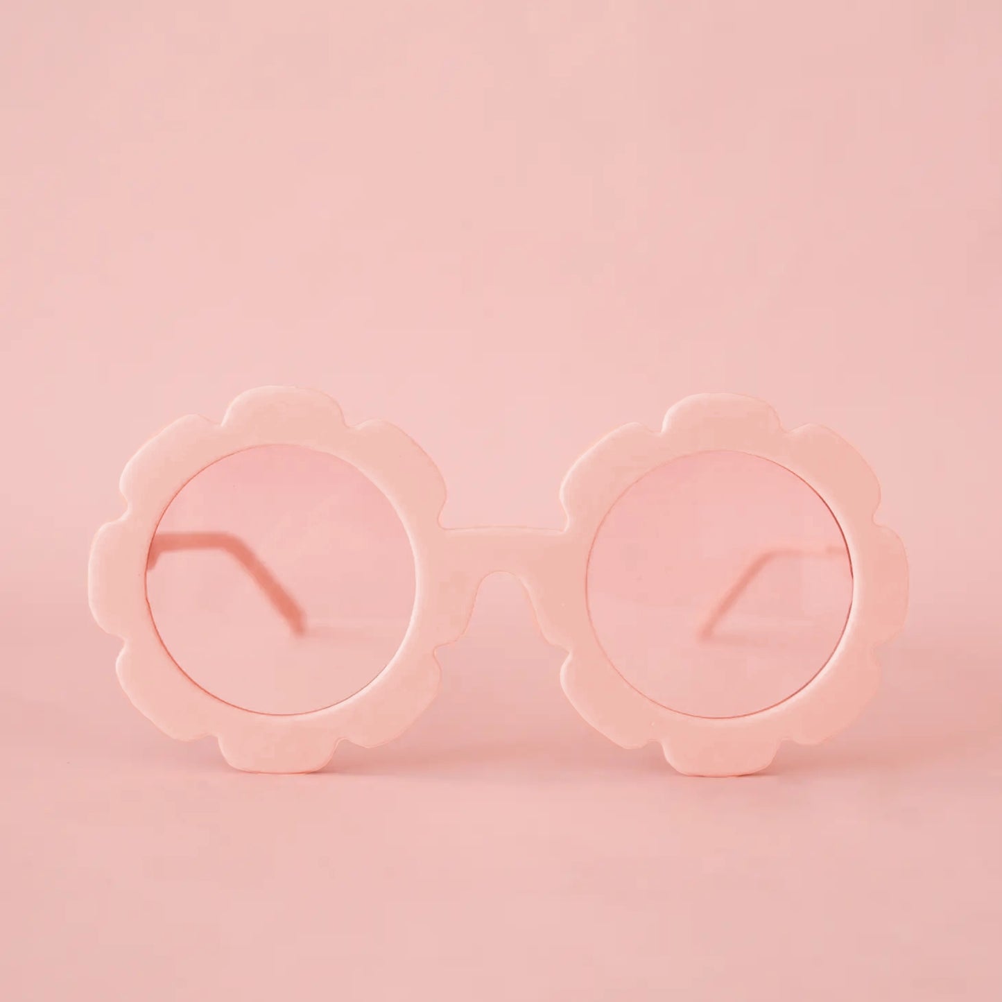 On a pink background is a pink pair of flower shaped sunglasses with a light pink circle lens in the center.