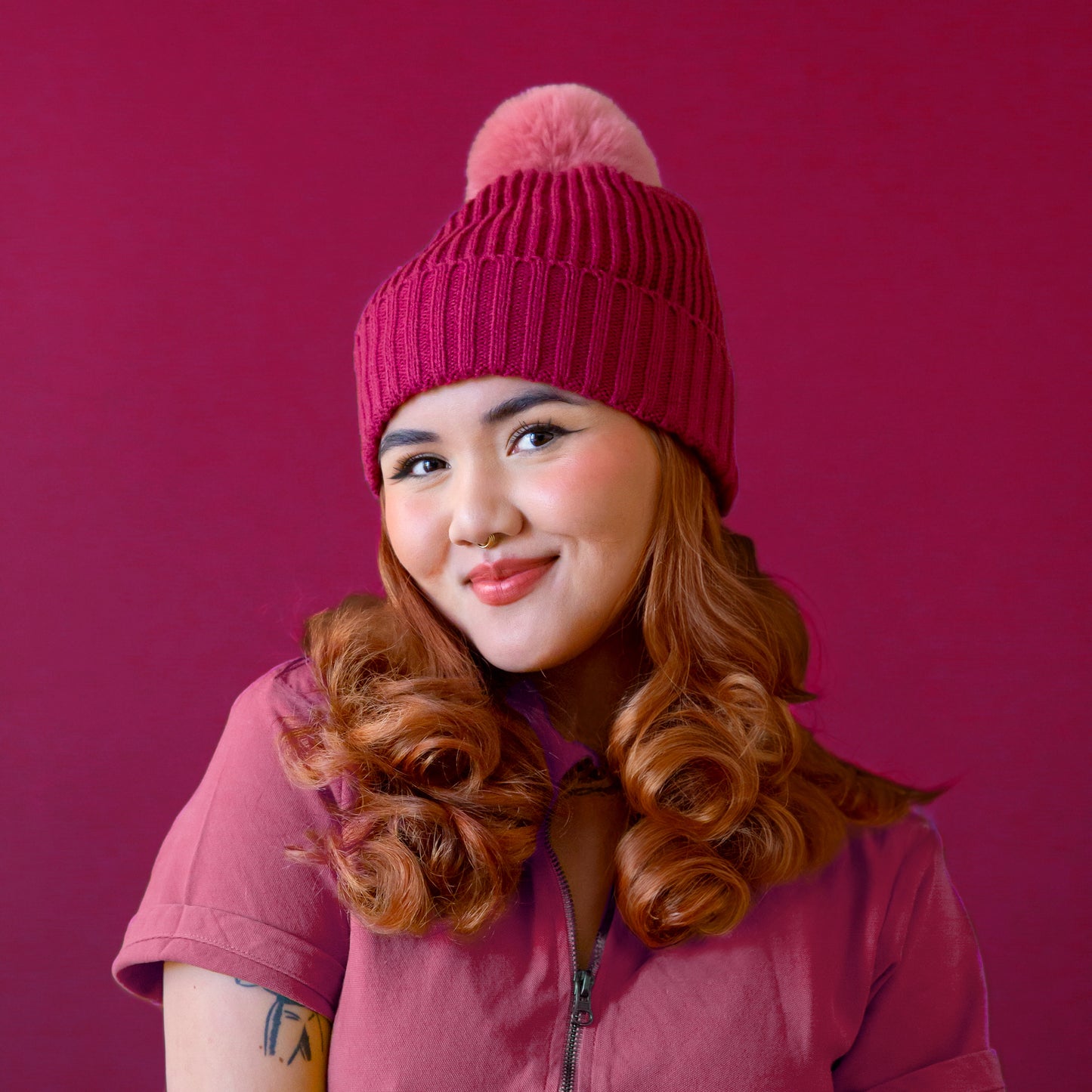 A model wearing a dark pink beanie with a lighter pink pom at the top.