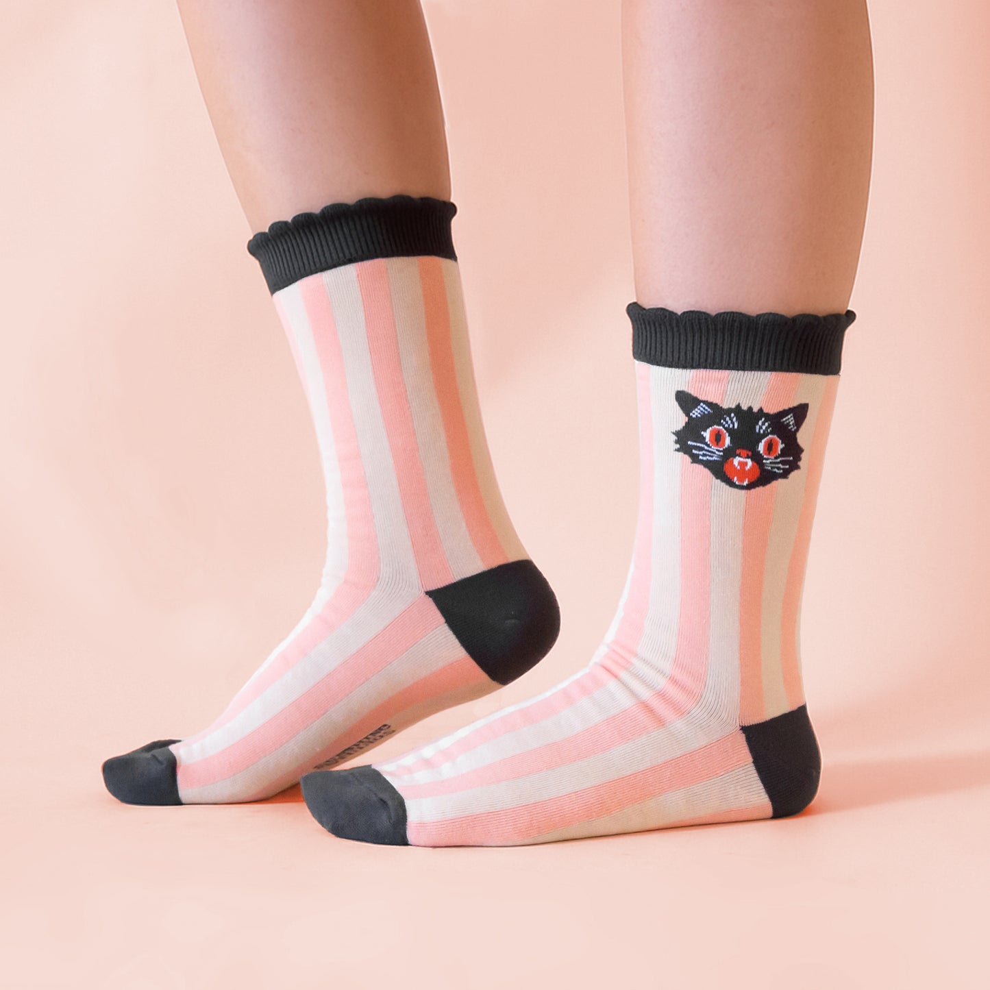 Feet wearing a pair of socks with peach colored stripes and a vintage illustration of a black cat.