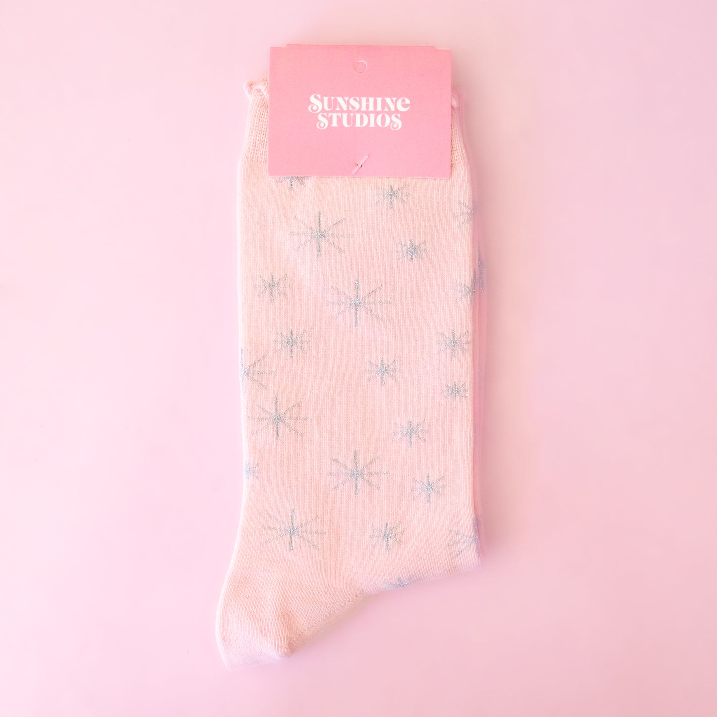 A pair of pink socks with silver stars folded with packaging on a pink background.
