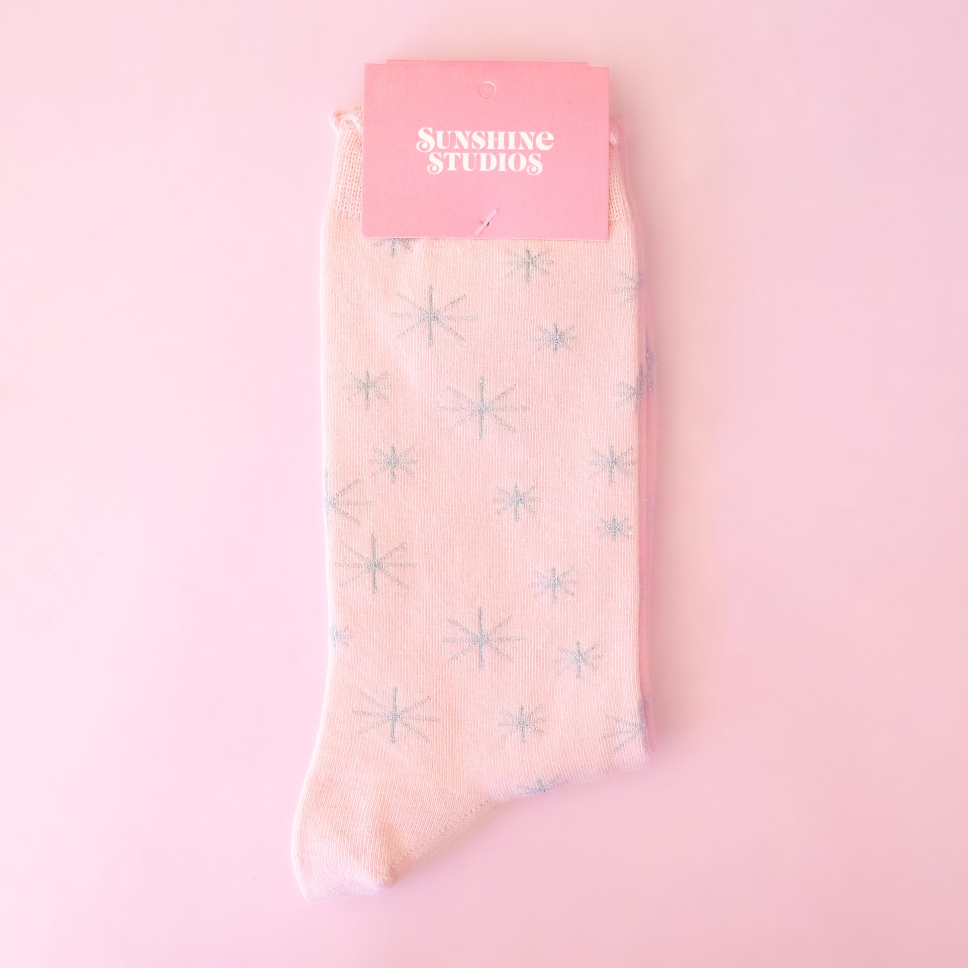 A pair of pink socks with silver stars folded with packaging on a pink background.