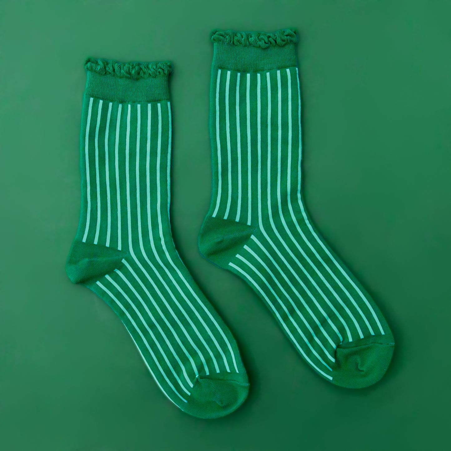 A pair of emerald green crew socks with a lighter green stripe and a ruffle edge at the top.