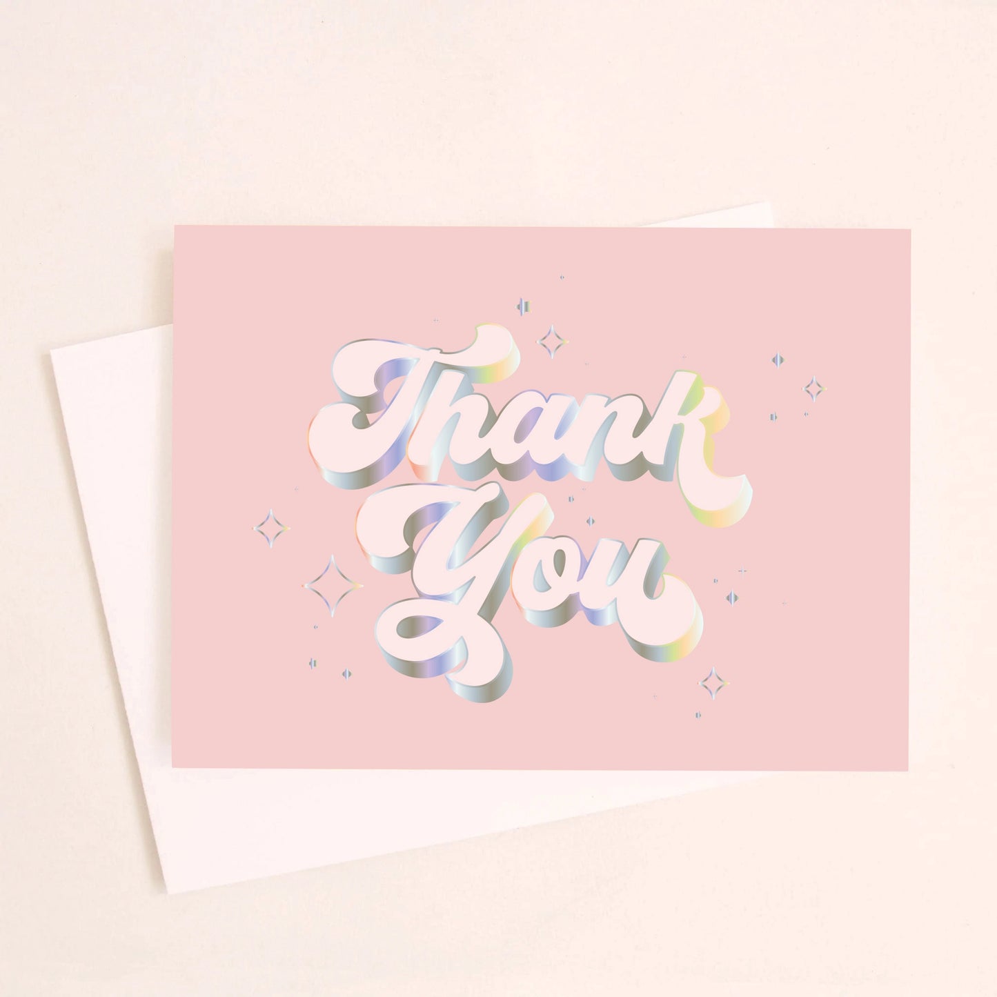 On an ivory background is a light pink card that reads, "Thank You" with in white text with holographic outlining.