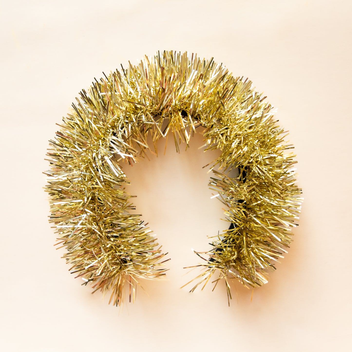 A gold tinsel headband sits on a soft yellow ground.