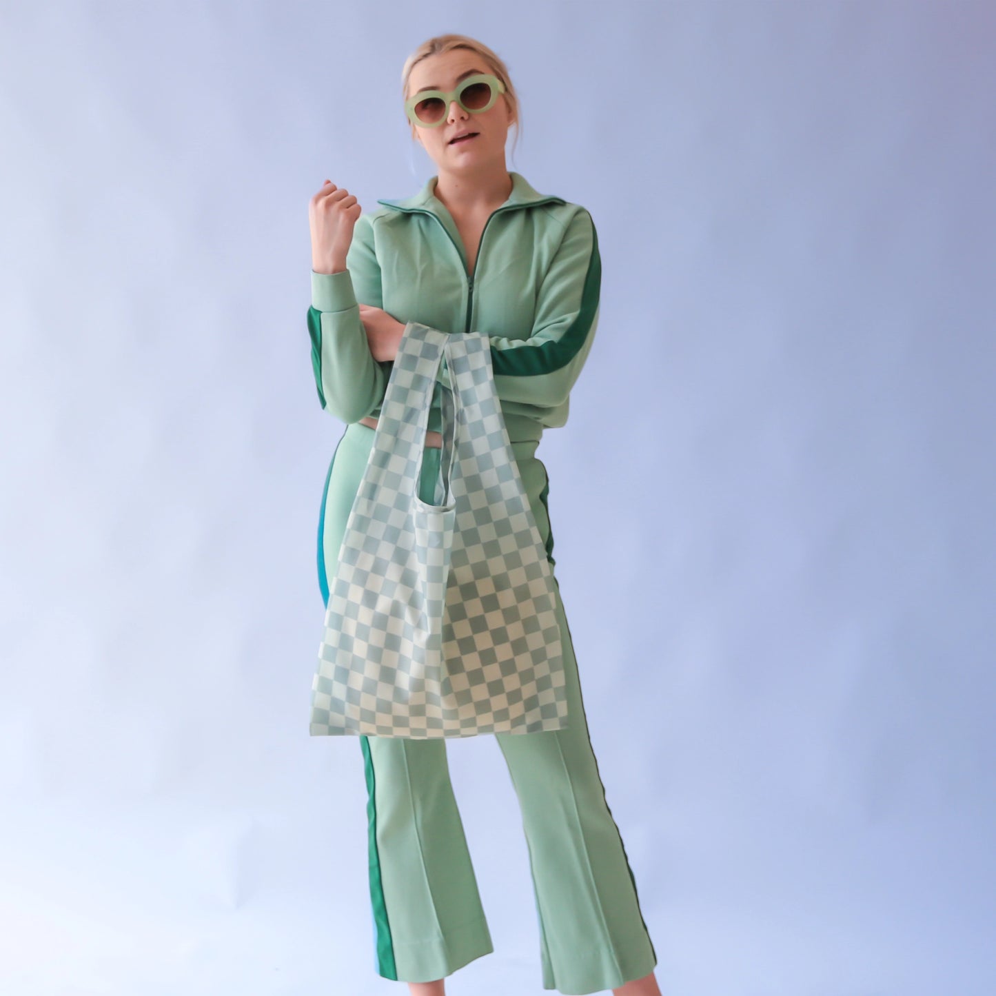 On a light blue background is a model holding an aqua colored nylon tote with a checkered print all over.