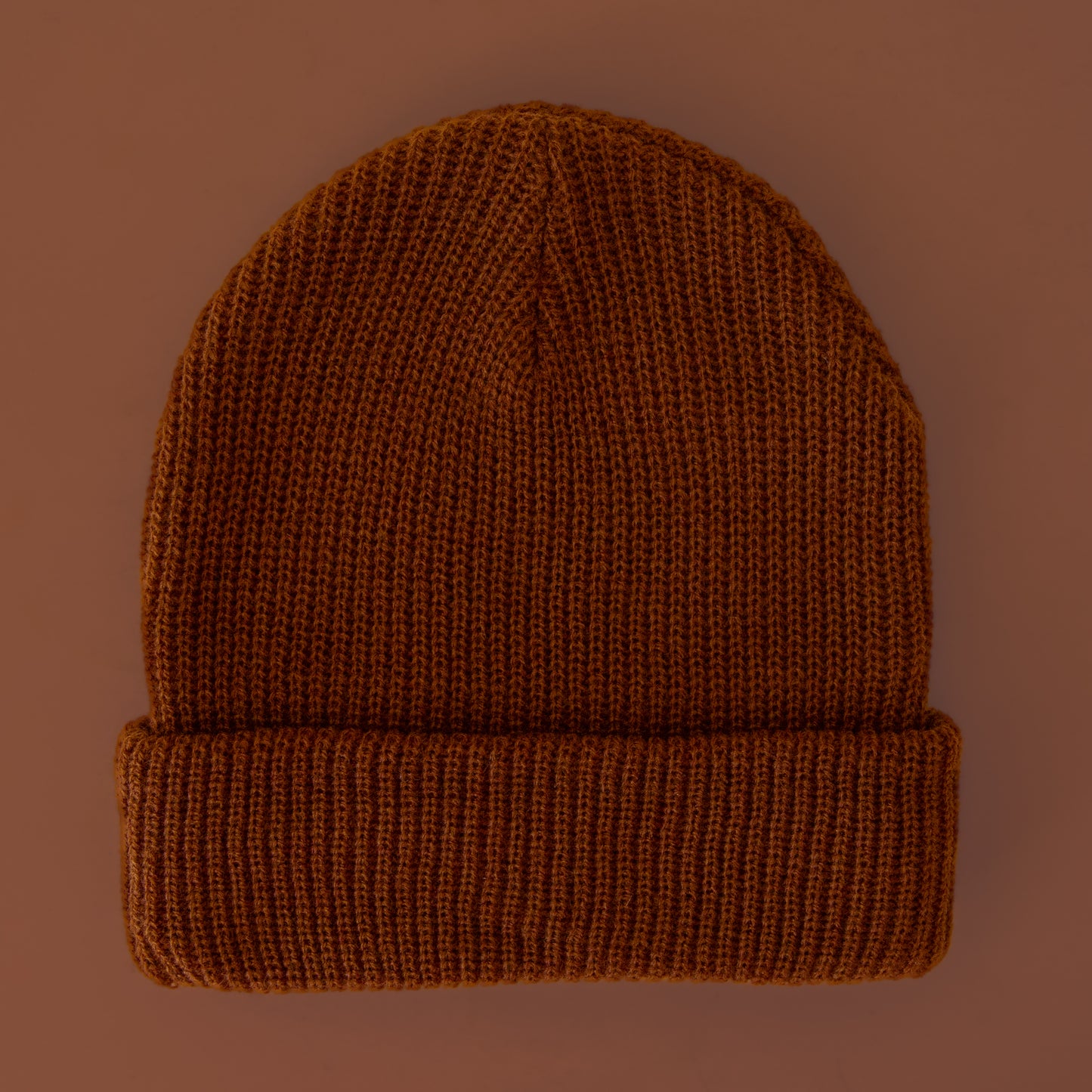 A brown knit beanie sits on a brown colored background.
