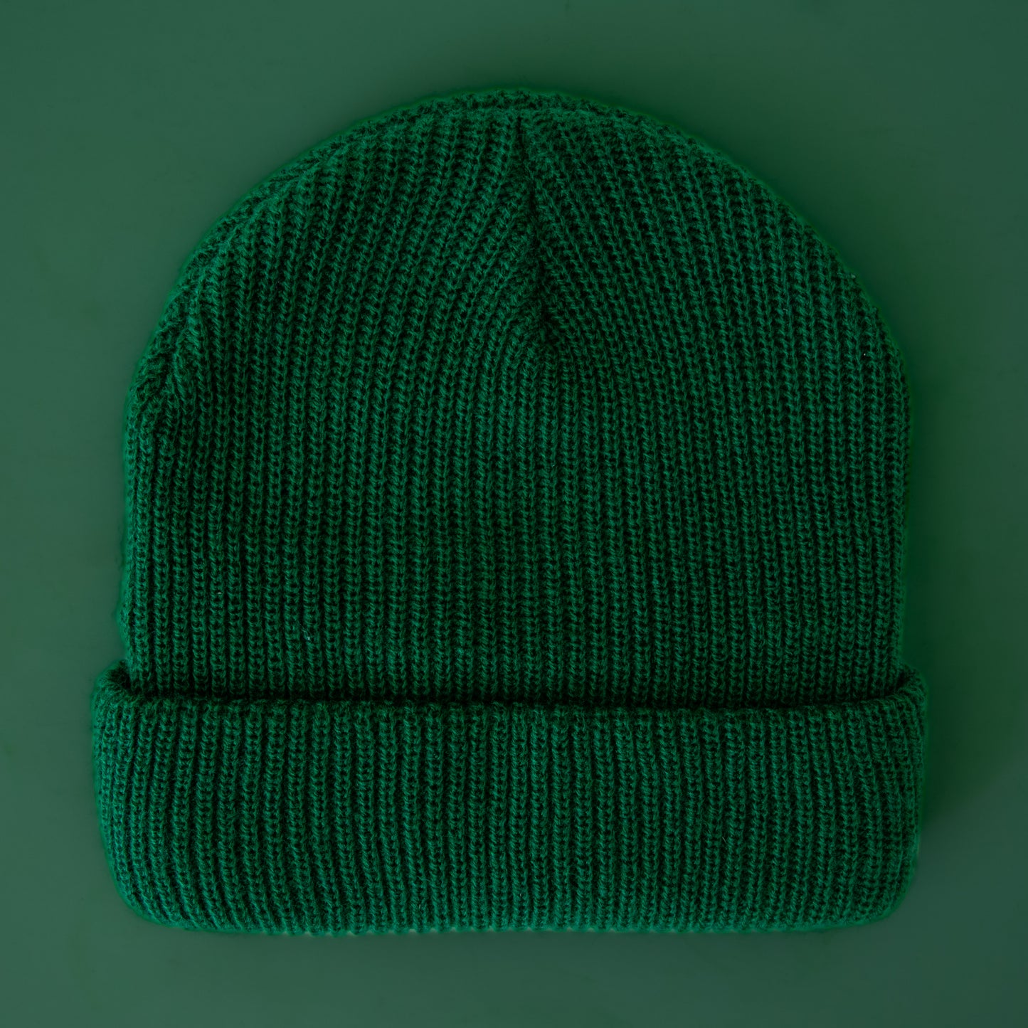 An emerald colored knit beanie sits on a green background.
