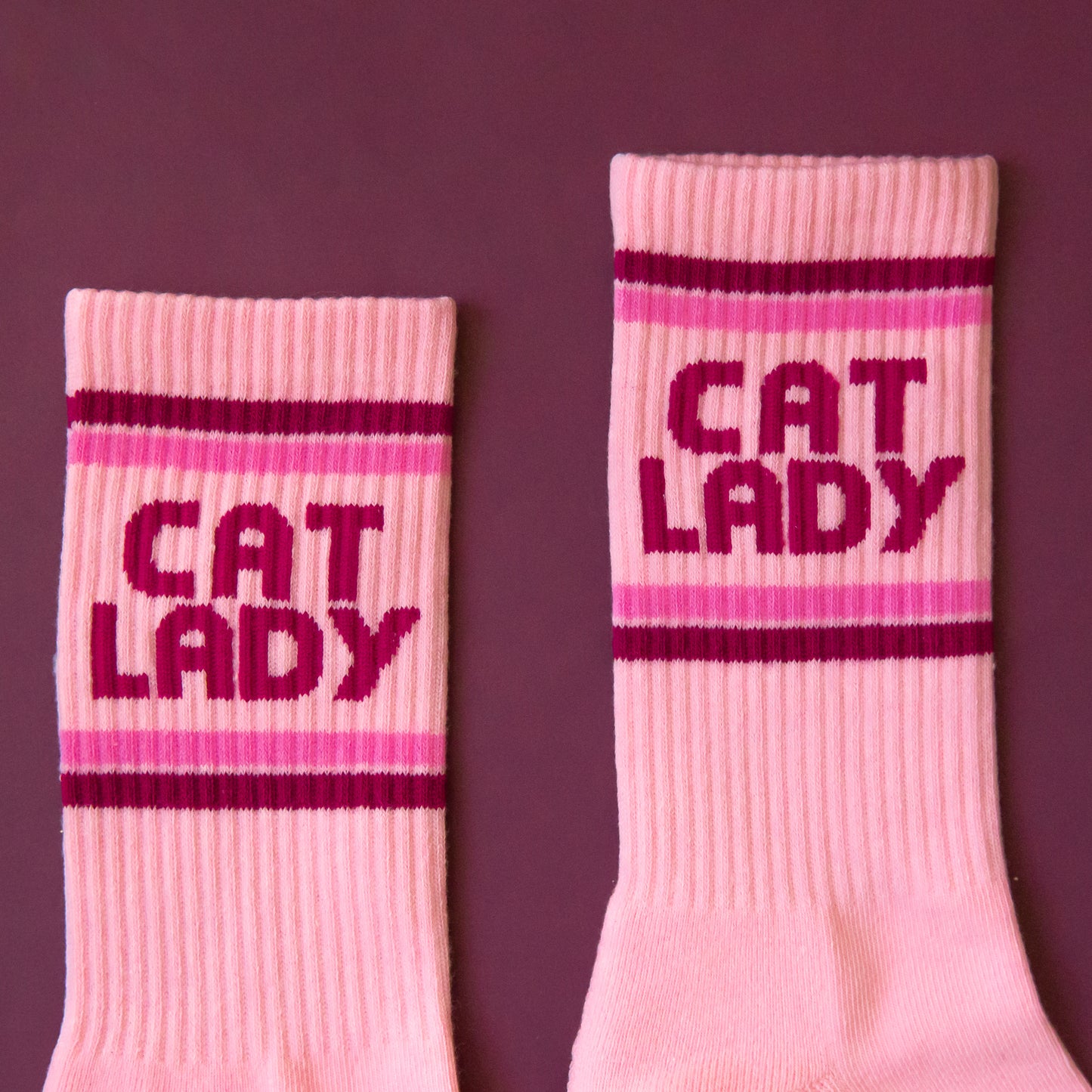 A pair of pink socks with dark pink text on the ankle of the sock that reads, 'Cat Lady'.