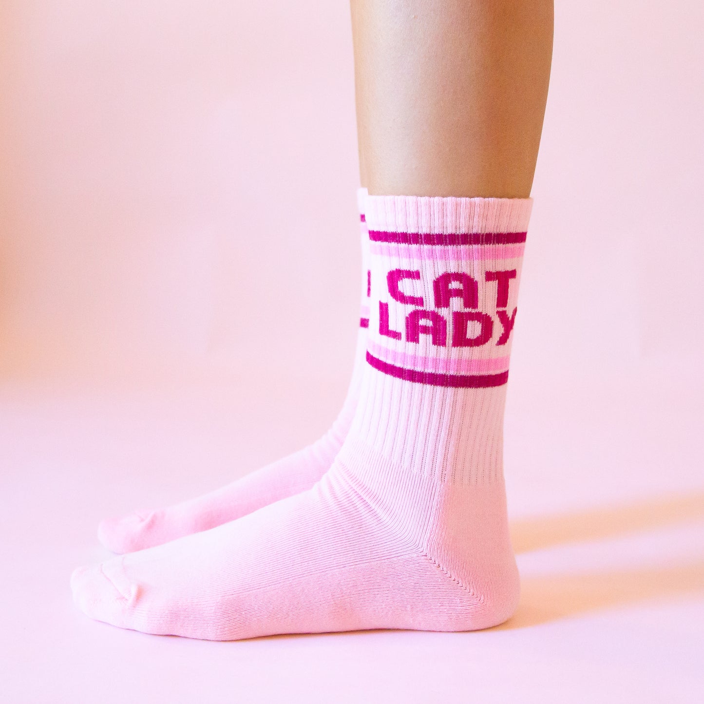A pair of pink socks with dark pink text on the ankle of the sock that reads, 'Cat Lady'.