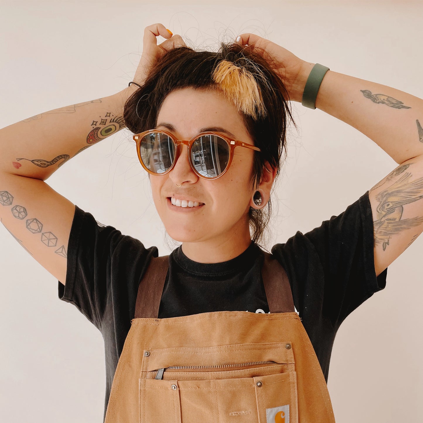 On a ivory background is a model wearing a round burnt orange, brownish pair of sunglasses with a grey lens.