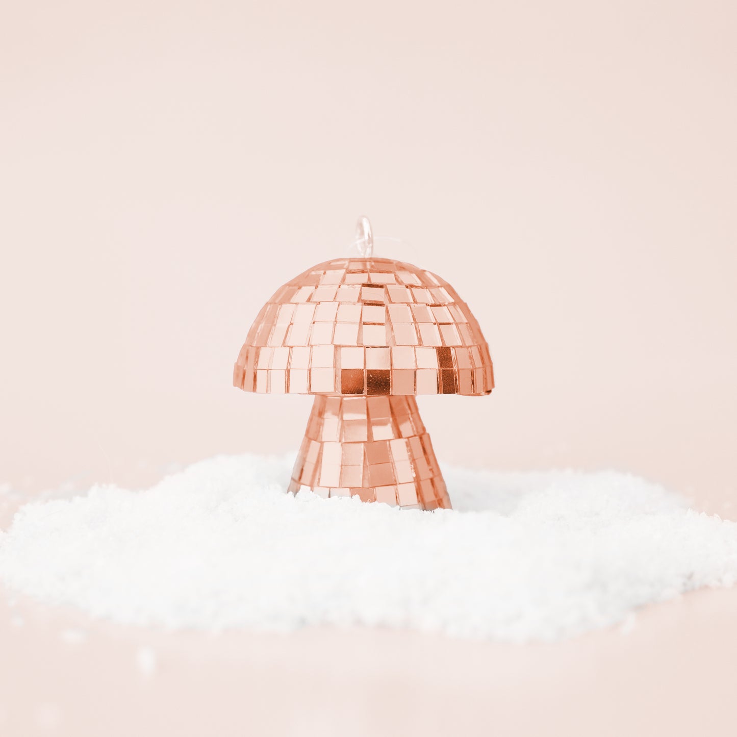 On a neutral snowy background is a rose gold disco mushroom shaped ornament.
