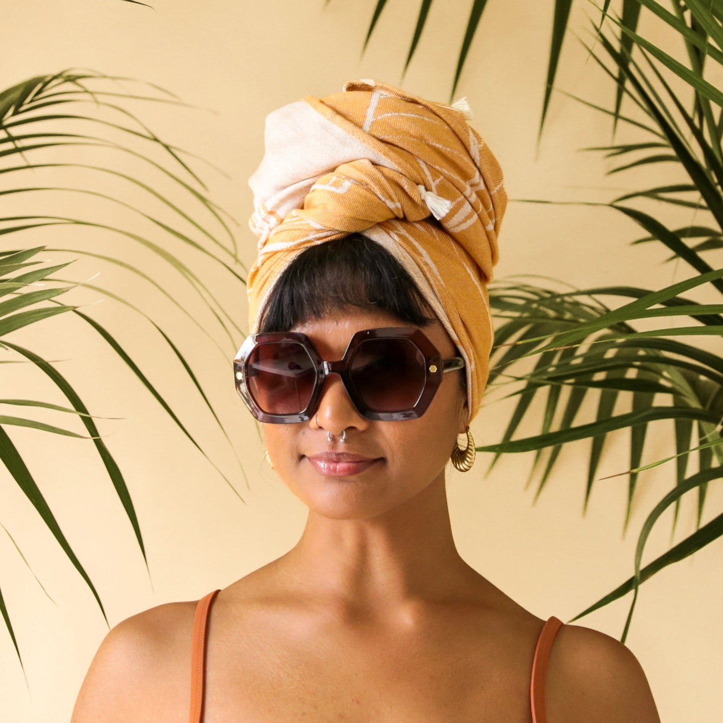 On a peachy background is a pair of hexagon shaped sunglasses in a cognac brown color.