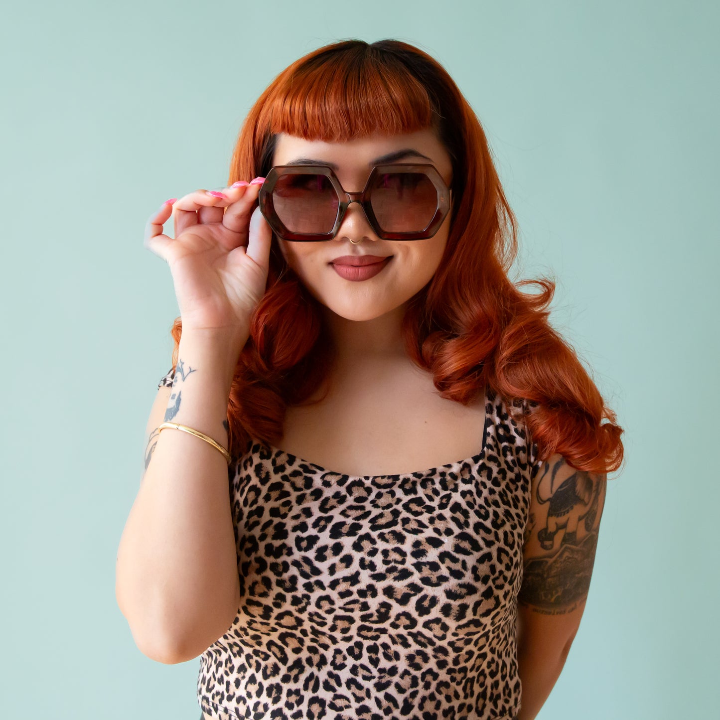 On a peachy background is a pair of hexagon shaped sunglasses in a cognac brown color.