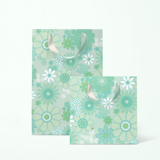 On a white background is a rendering of two gift bags with a mint and white floral print and ribbon handles.