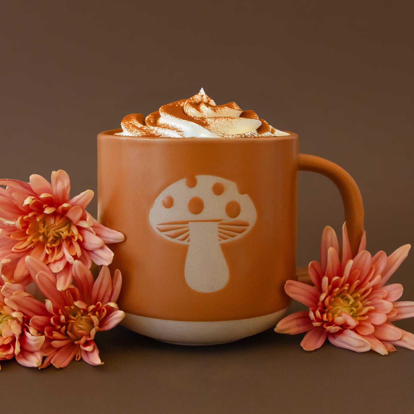 On a pink background is a ceramic mug with a light colored mushroom design.
