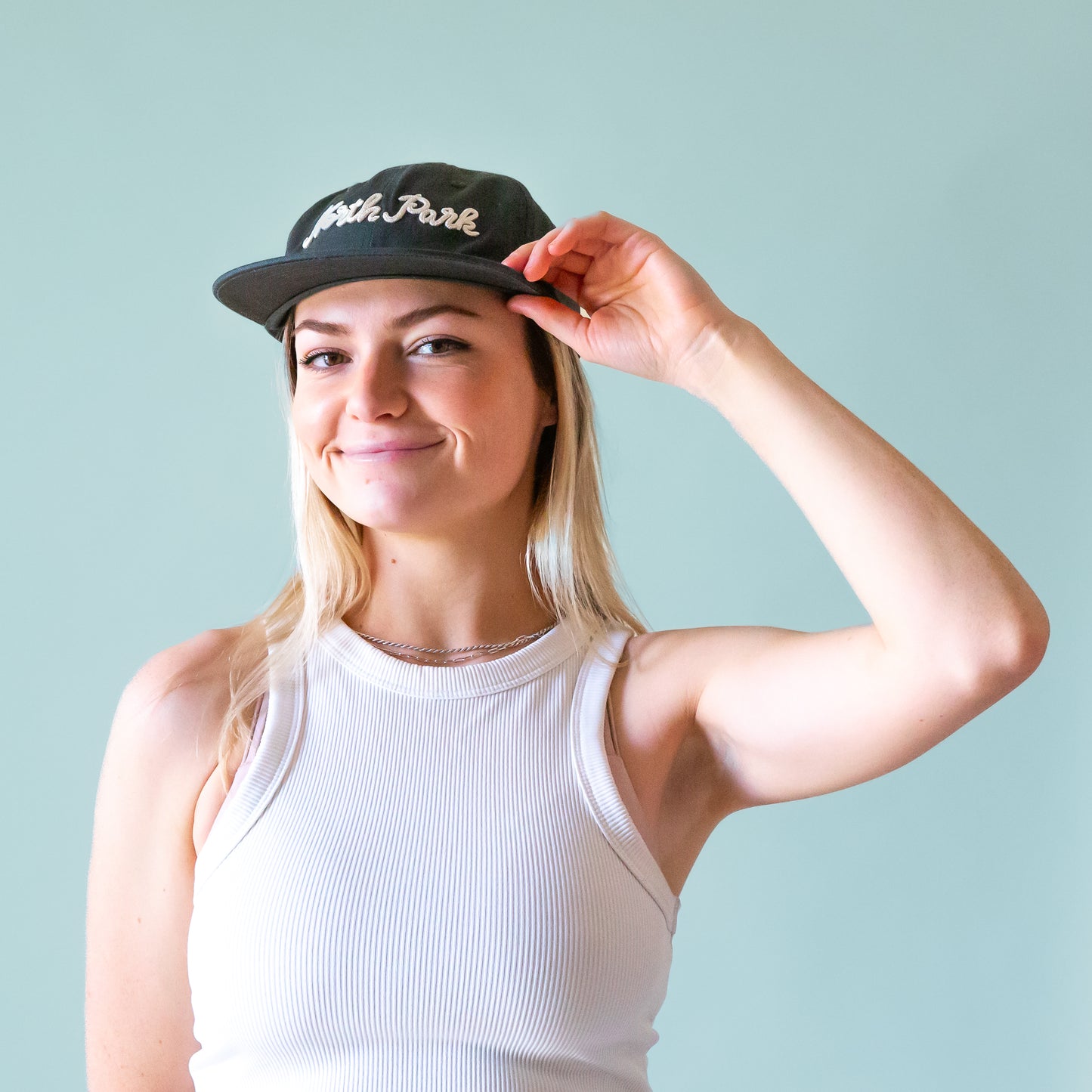 A dark greenish blue flat brim hat with white embroidered text that reads, 'North Park'.