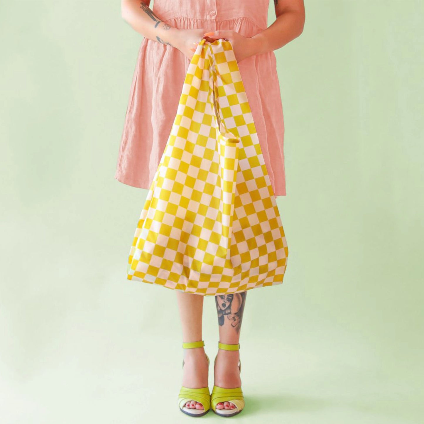 On a light green background is light green and ivory checkered reusable nylon bag in a model's hand.